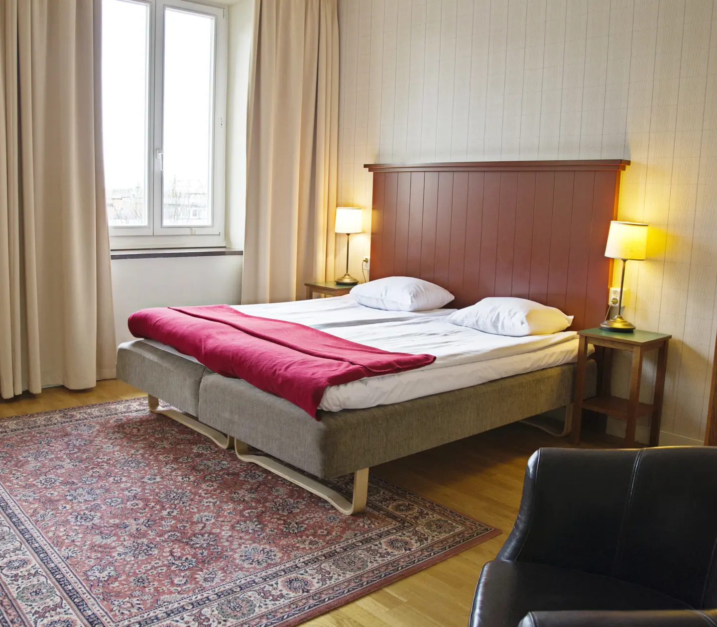 Mysigt hotellrum med säng, sänggavel i trä och svart läderfåtölj
