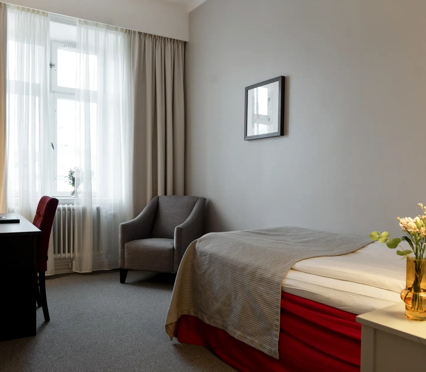 Mysigt hotellrum med enkelsäng, röd sänggavel, nattduksbord och spegel
