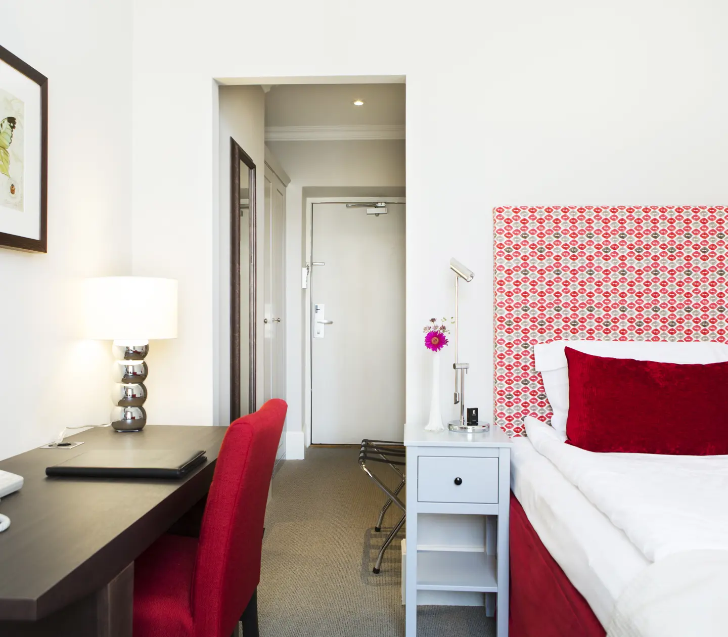 Mysigt hotellrum med enkelsäng, skrivbord, fåtölj, tv och fönster