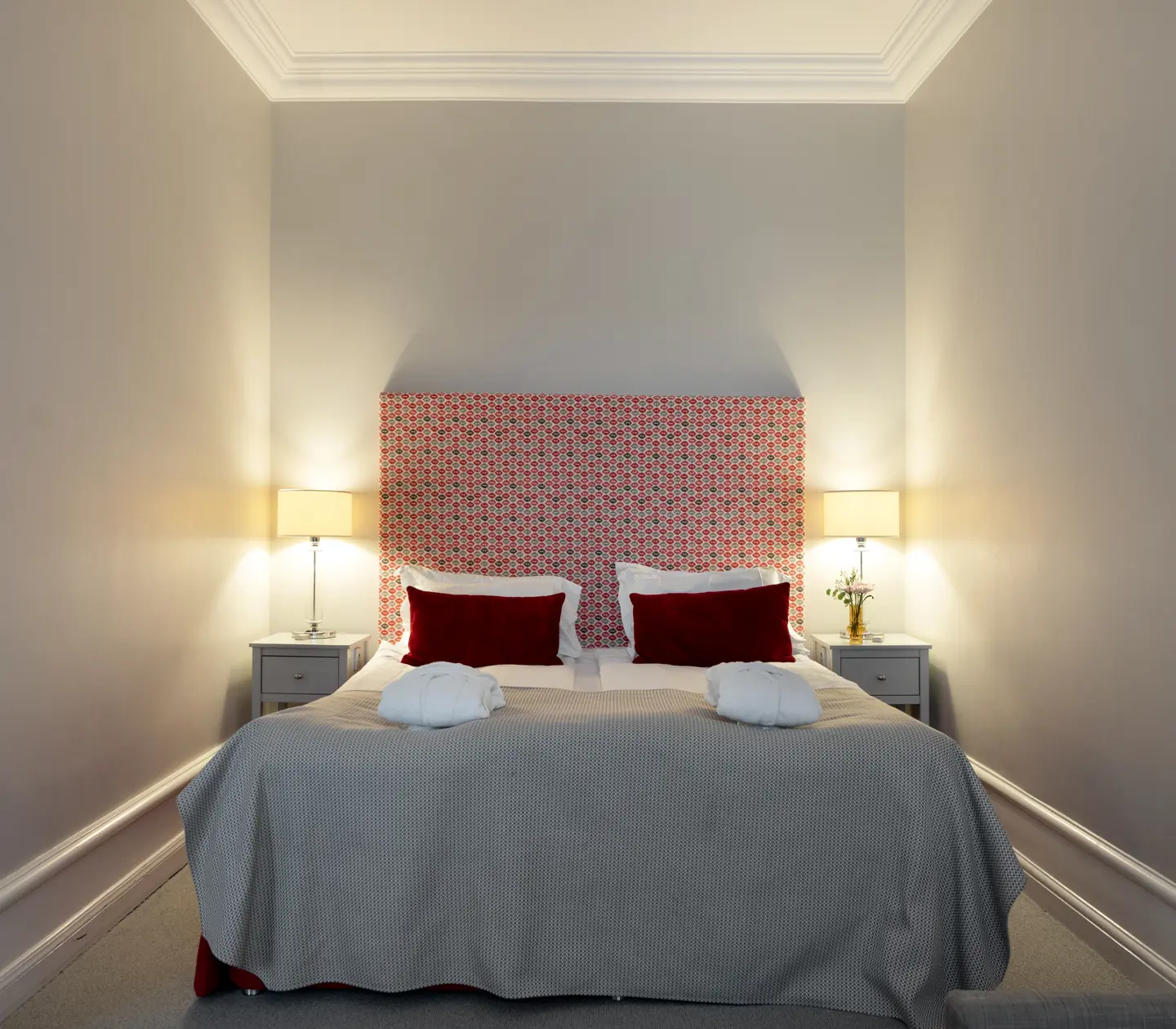 Hotellrum med dubbelsäng, röd sänggavel och sänglampor