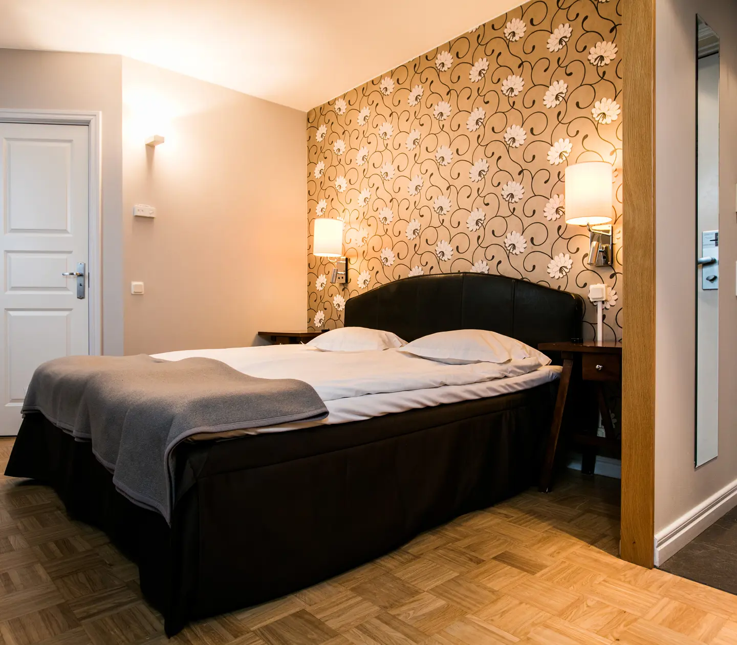 Hotellrum med dubbelsäng, sänglampor och spegel