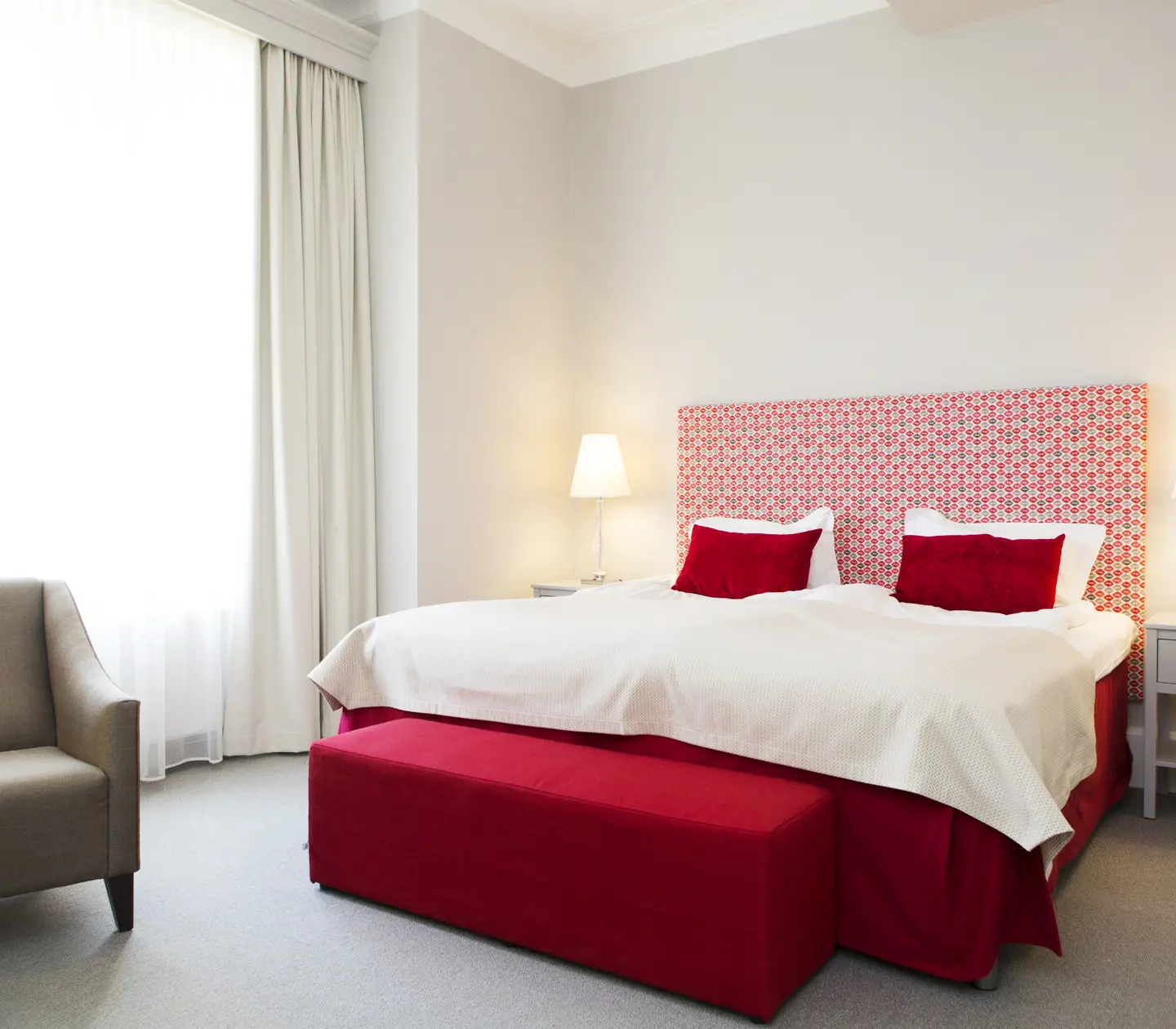 Ljust hotellrum med säng, röd sänggavel och fåtölj