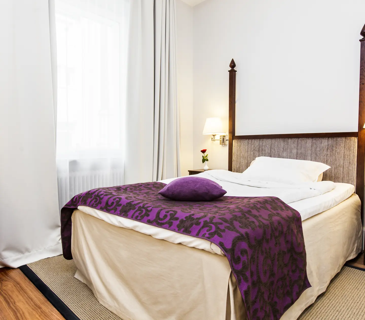 Ljust hotellrum med fönster, enkelsäng och sänglampor