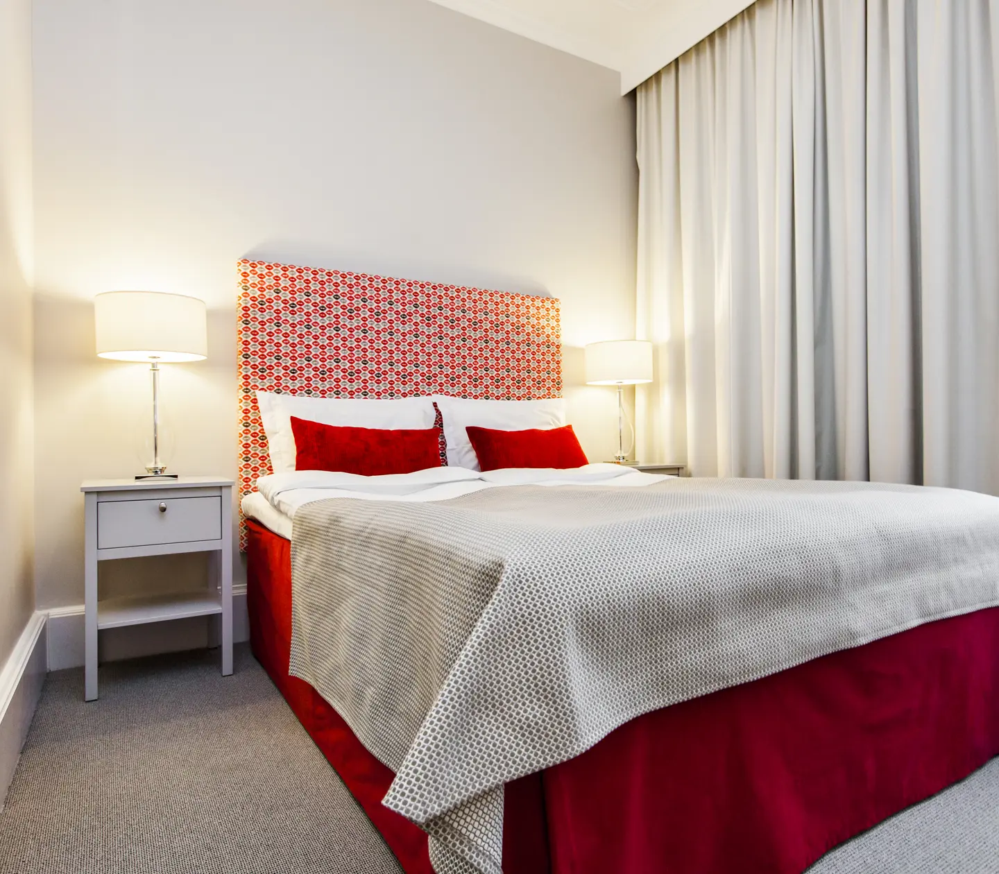 Ljust hotellrum med enkelsäng, röd sänggavel och sänglampor