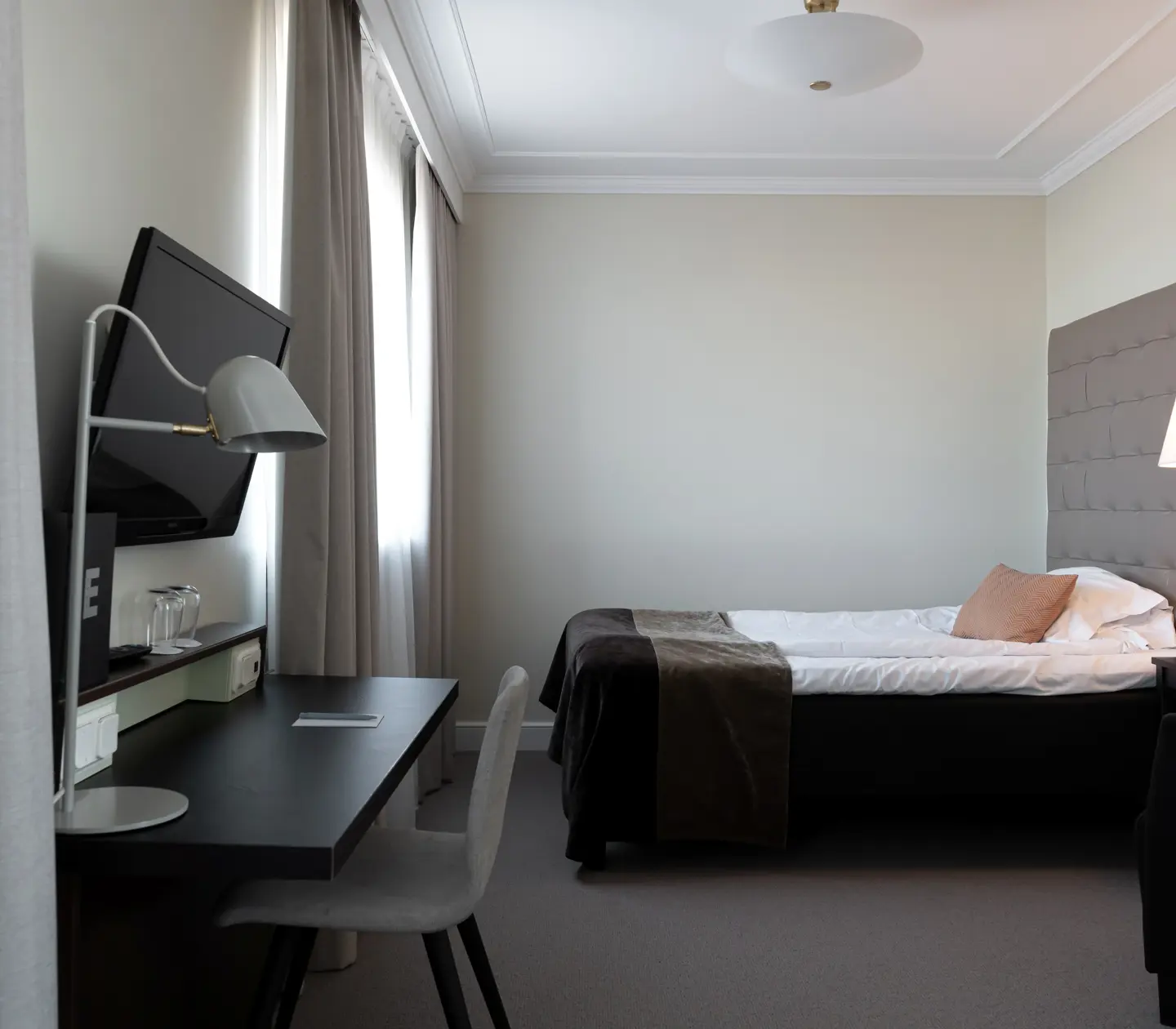 Ljust hotellrum med skrivbord, säng och sänglampa