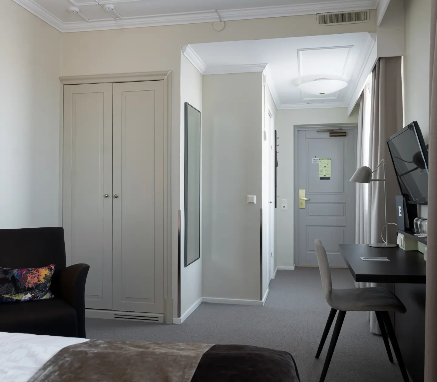Ljust hotellrum med skrivbord, garderob och fåtölj