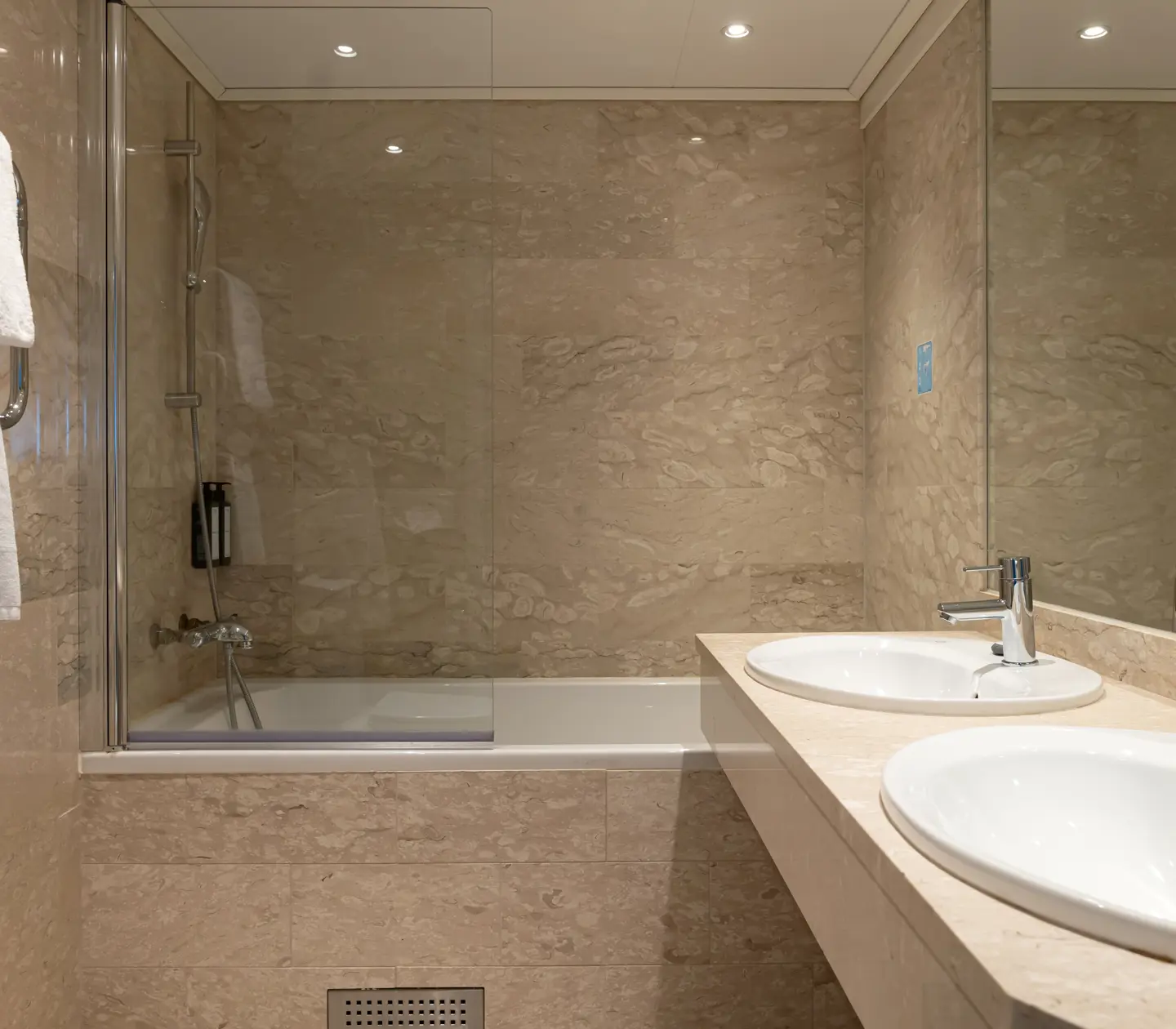 Beige badrum med dubbla handfat, badkar och spegel