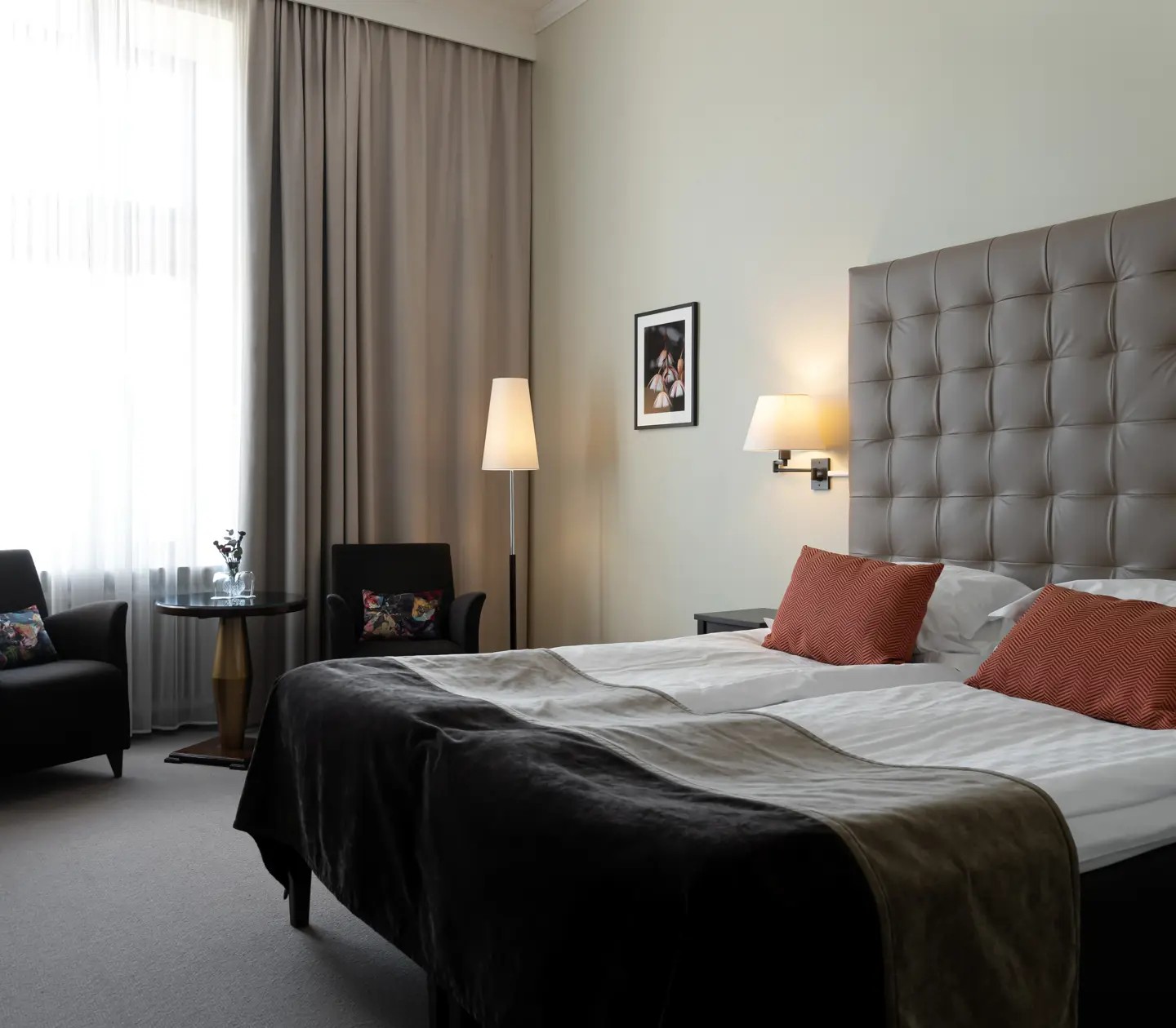 Ljust hotellrum med säng, stor sänggavel och fåtöljer