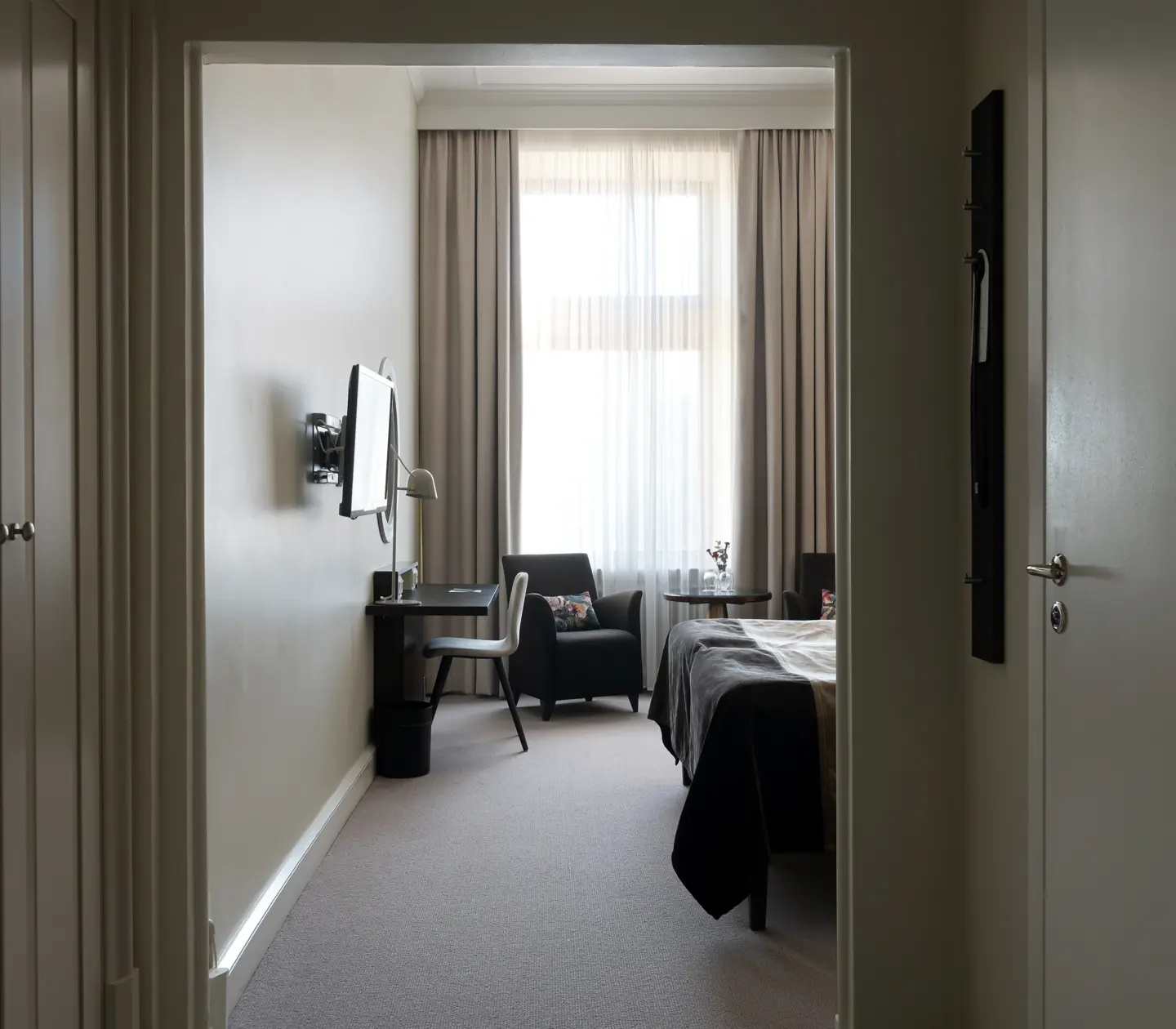 Ljust hotellrum med skrivbord, garderob och fåtölj