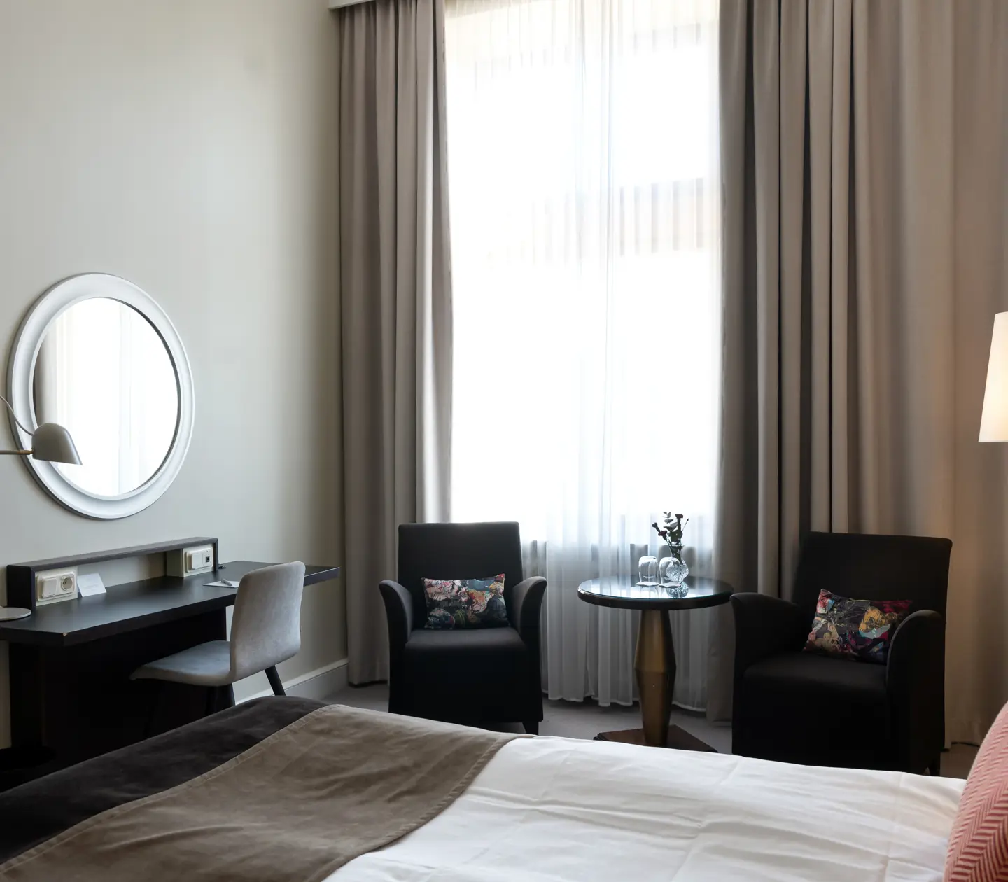 Ljust hotellrum med skrivbord, fåtöljer och fönster