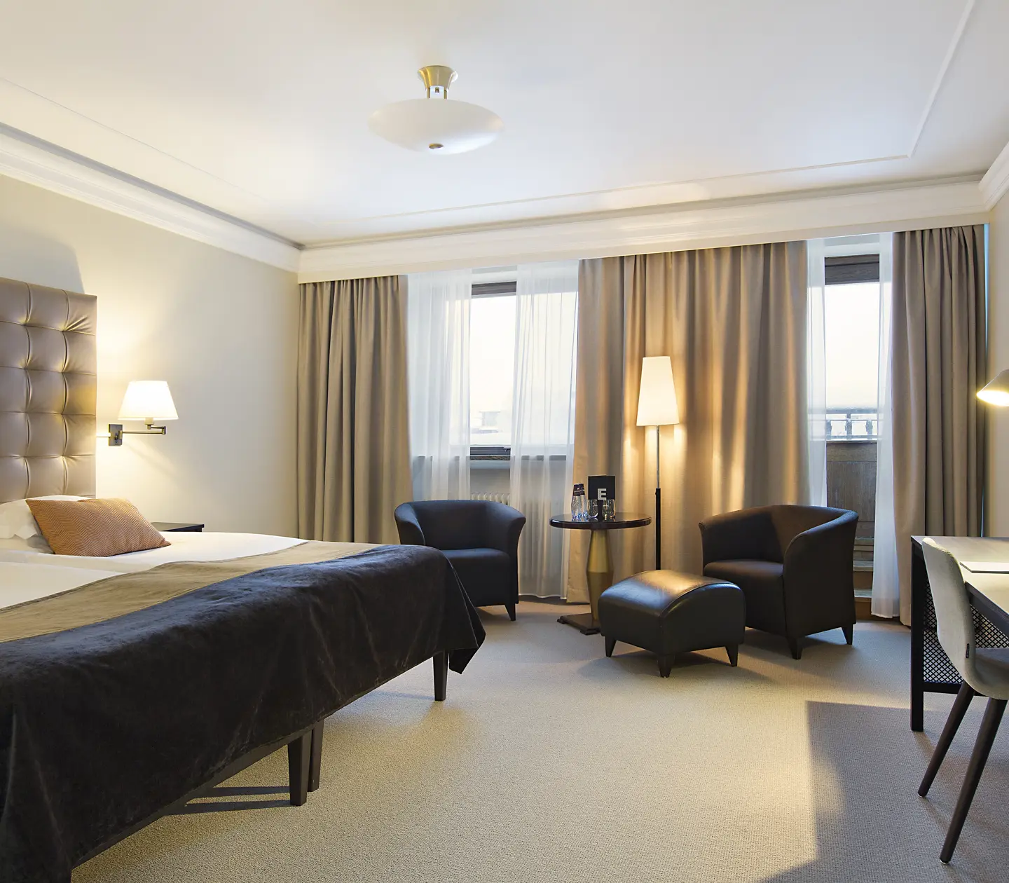 Ljust hotellrum med säng, fåtöljer och skrivbord
