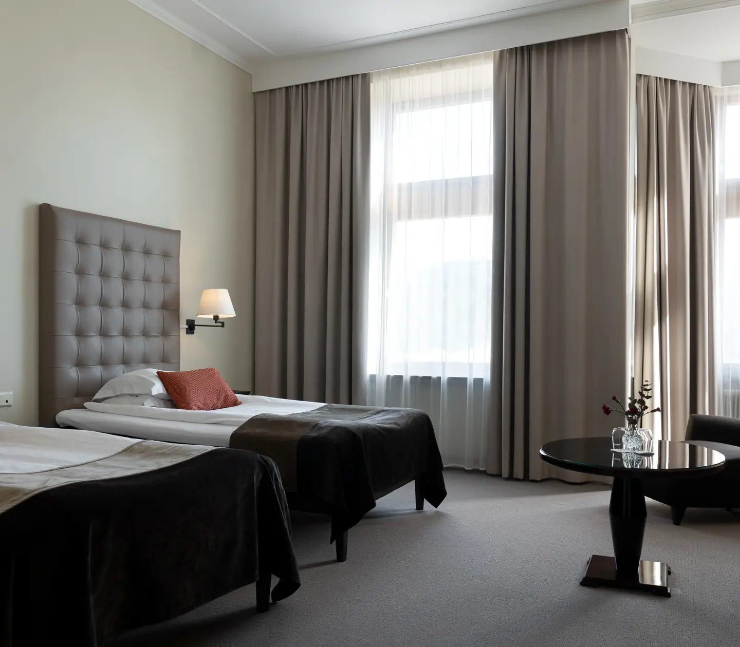 Ljust hotellrum med två enkelsängar, sittgrupp och stora fönster