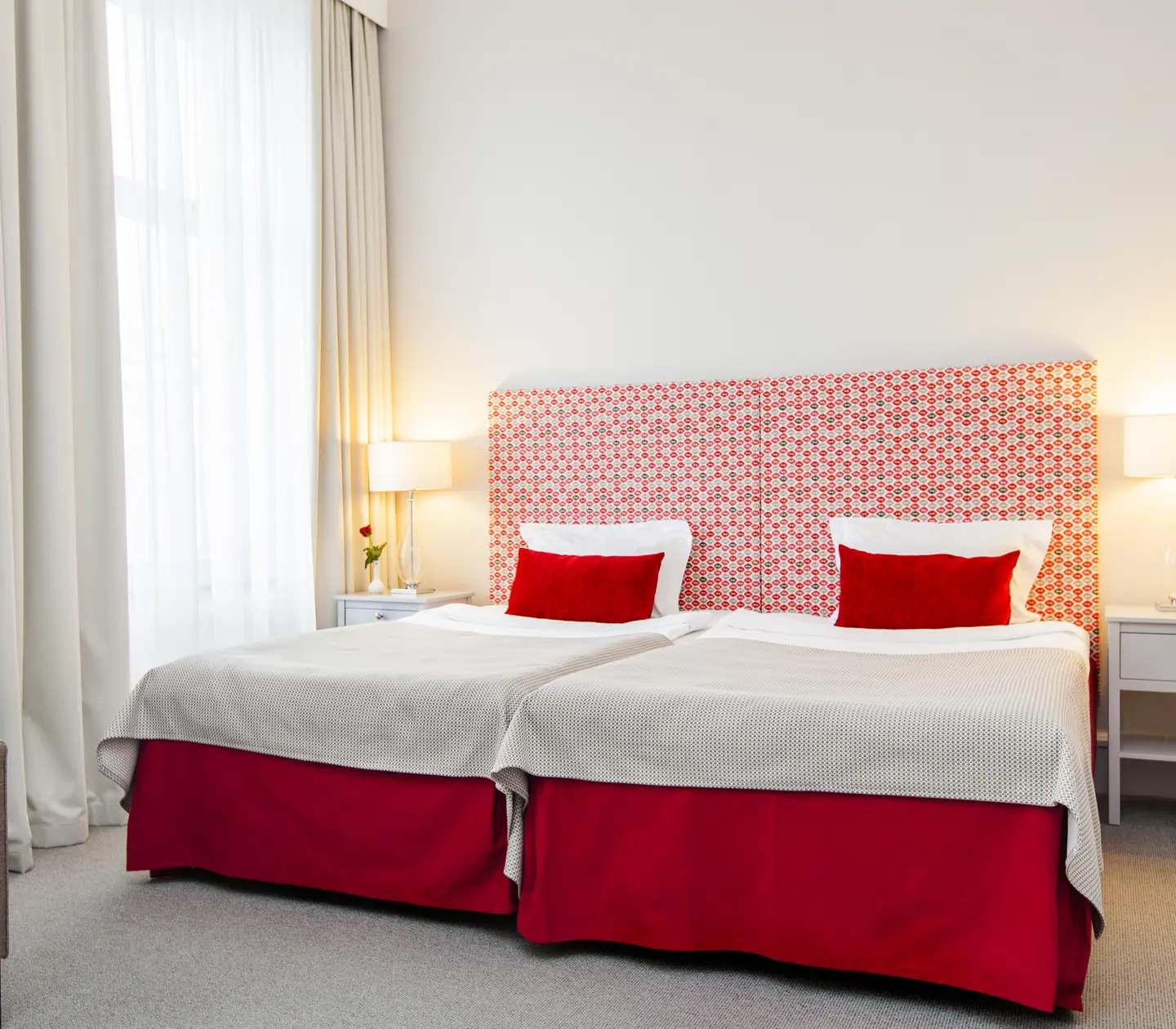 Ljust hotellrum med säng, röd sänggavel och fåtölj