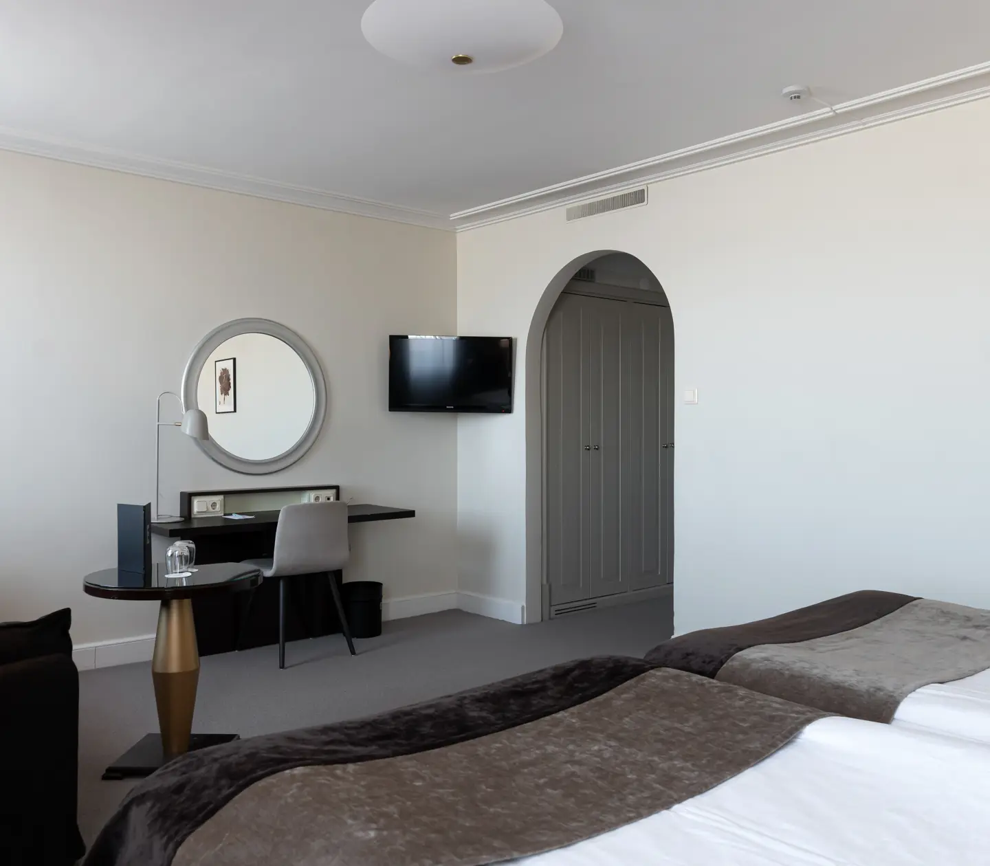 Ljust hotellrum med valv, skrivbord och rund spegel