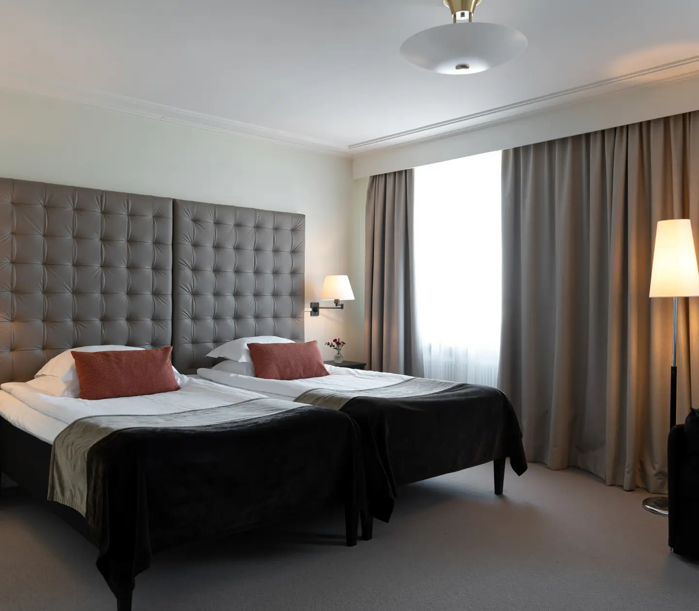 Ljust hotellrum med säng, stor sänggavel och gardiner