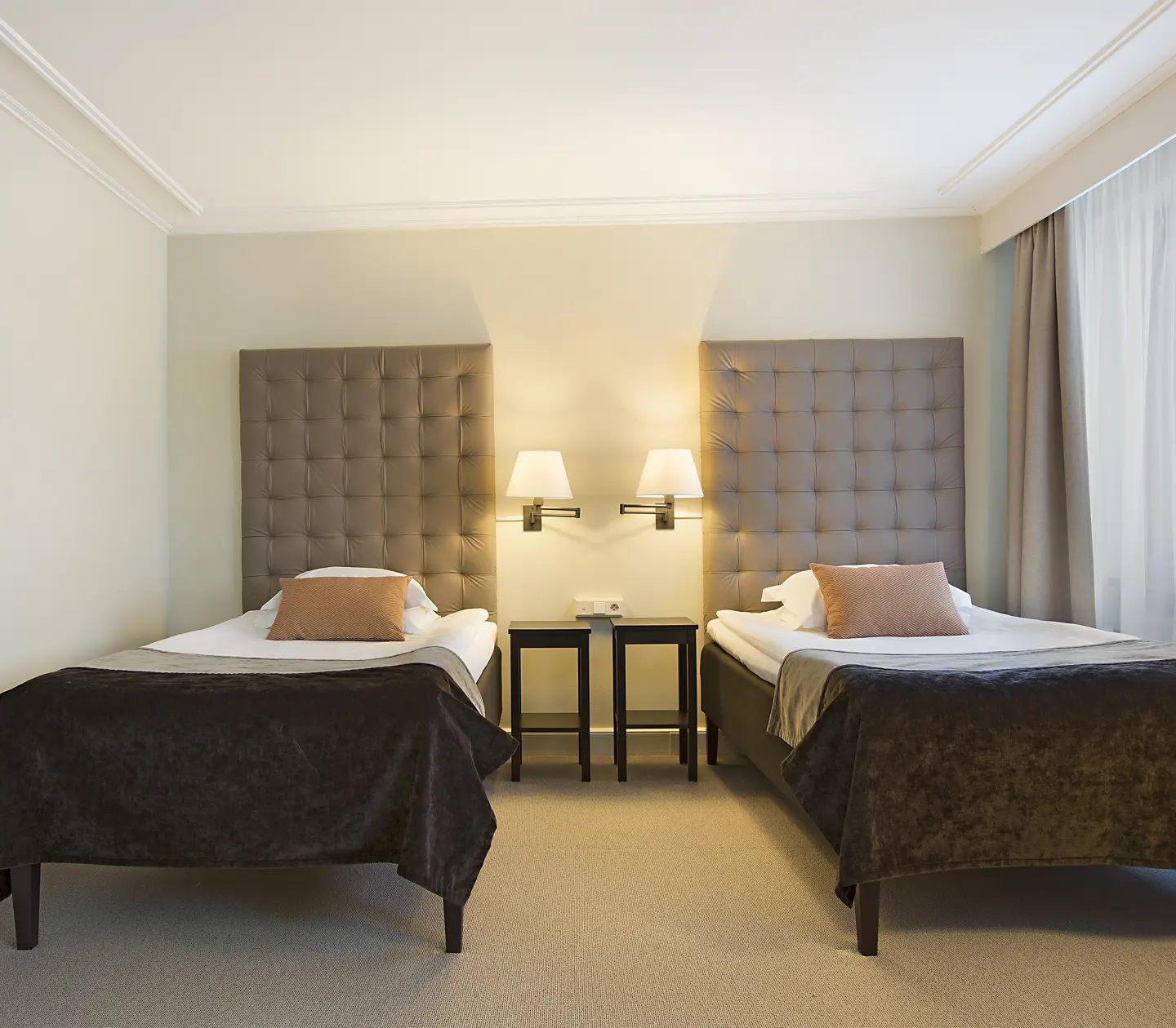 Ljust hotellrum med två sängar, sängbord och sänglampor
