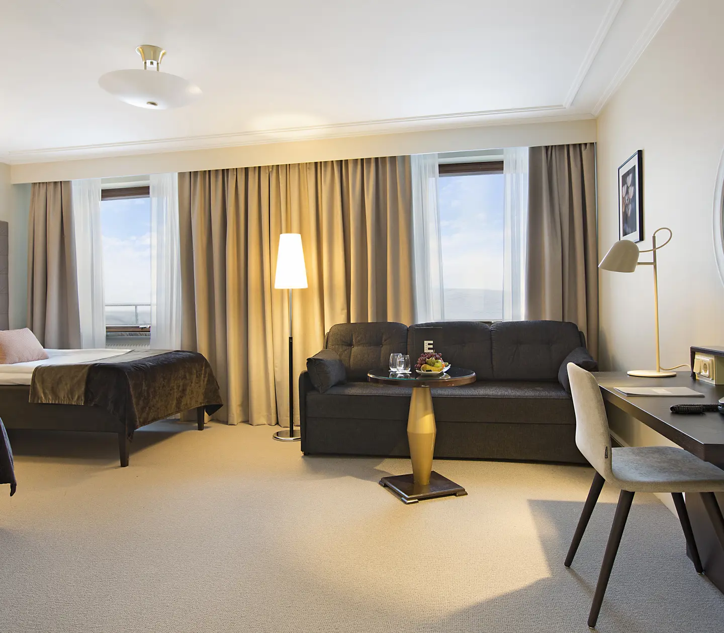Ljust hotellrum med två sängar, soffa och skrivbord