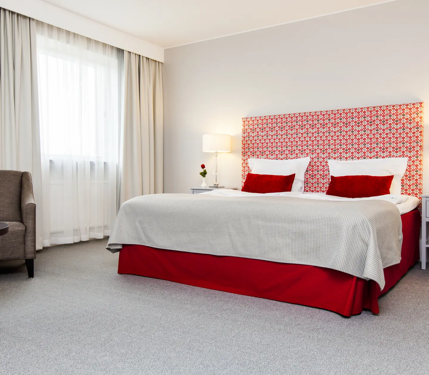 Ljust hotellrum med säng, röd sänggavel och fåtölj