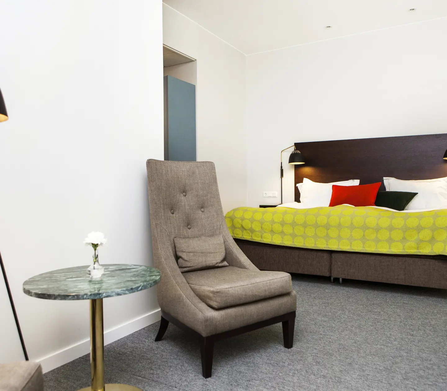Ljust hotellrum med säng, fåtölj och lampa