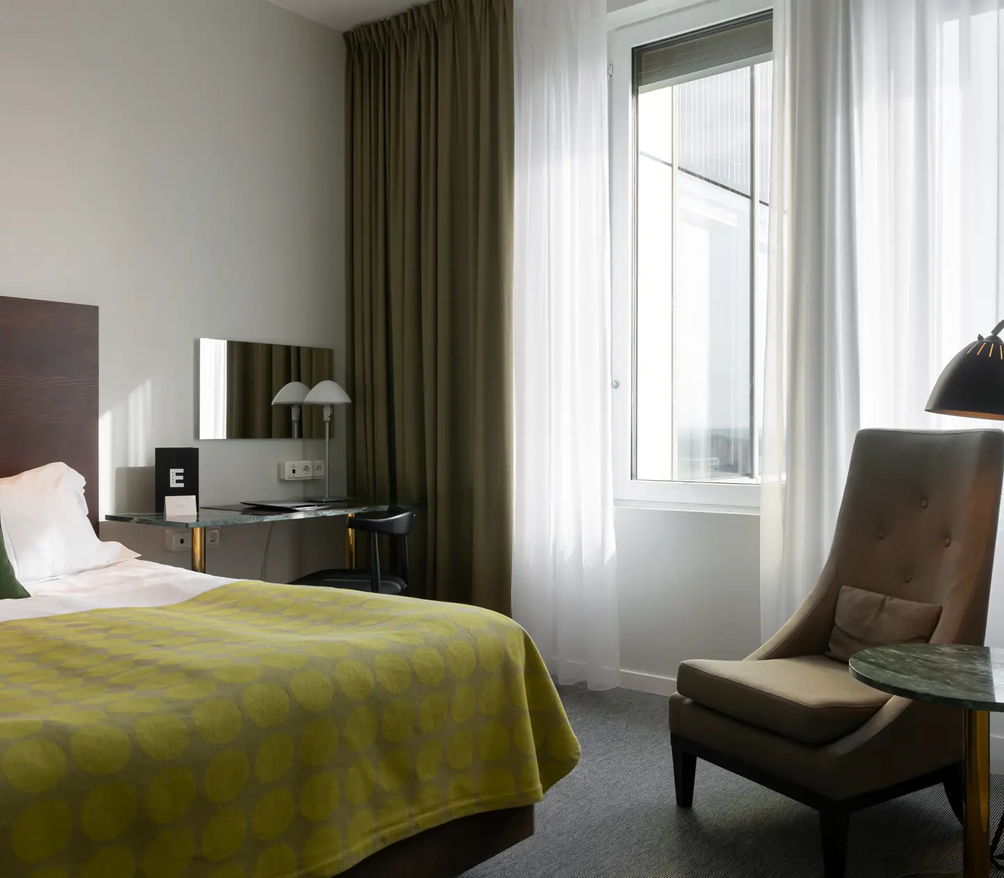Ljust hotellrum med säng, fåtölj och balkongdörr