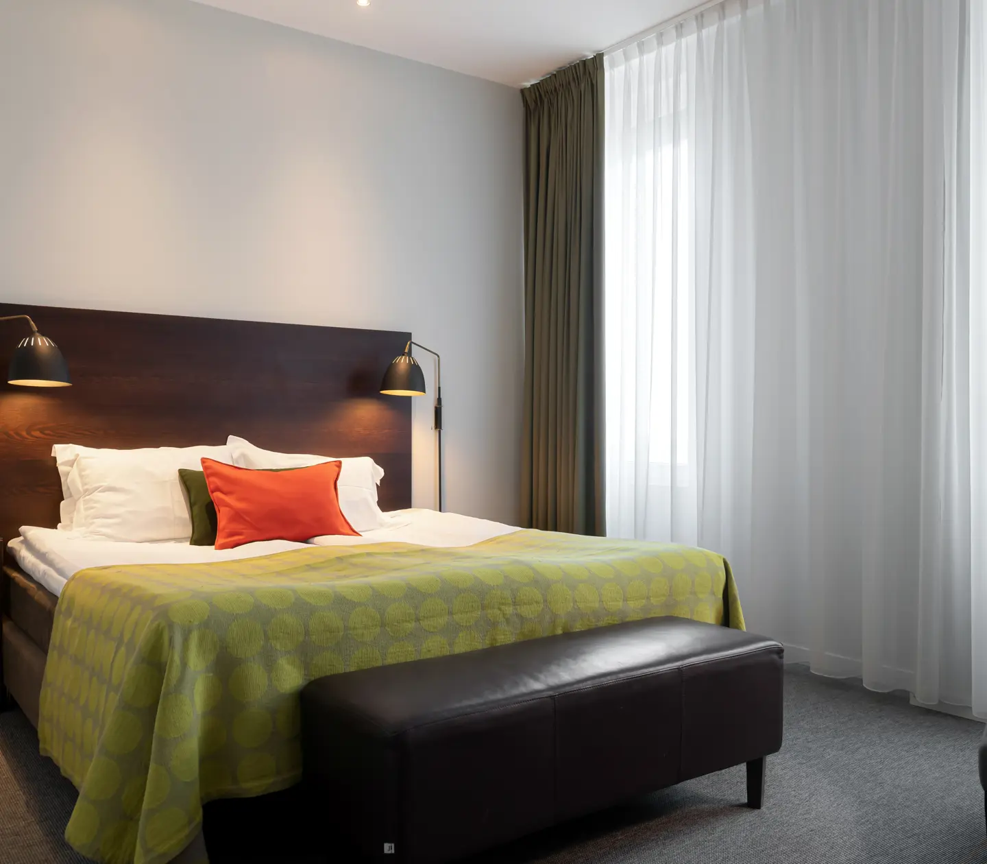 Ljust hotellrum med säng, fåtölj och fönster