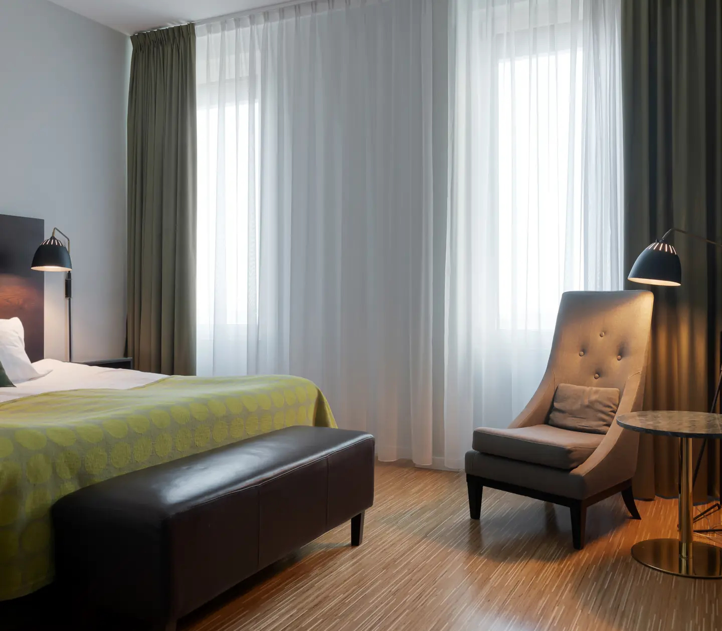 Ljust hotellrum med säng, fåtölj och fönster