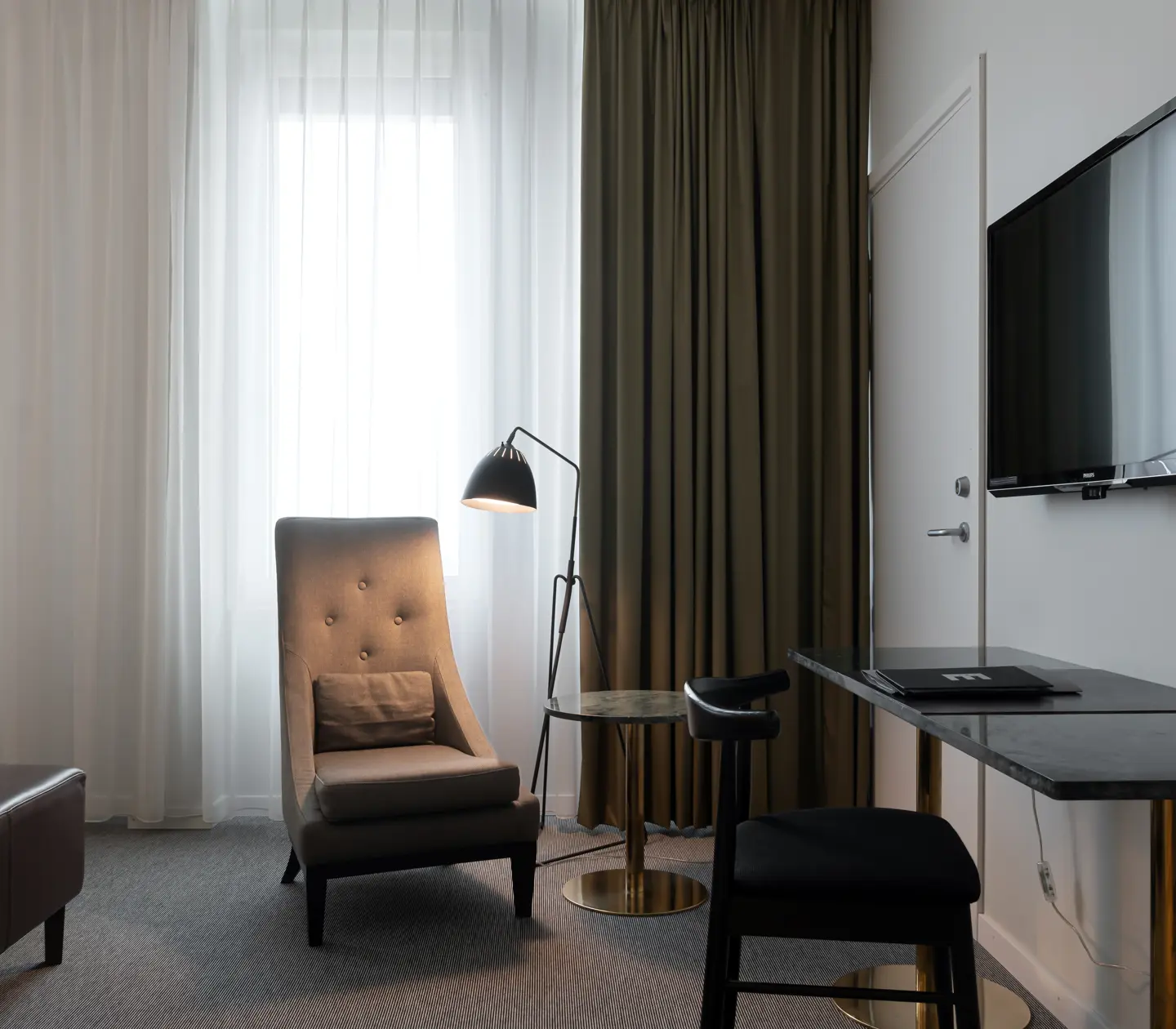 Ljust hotellrum med skrivbord, fåtölj och fönster