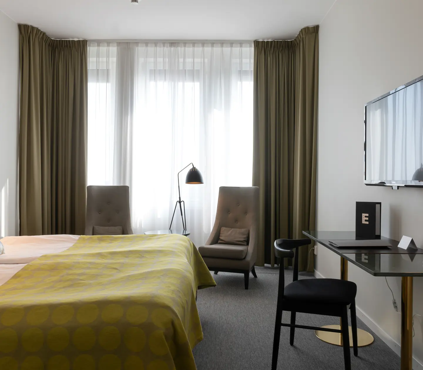 Ljust hotellrum med säng, fåtölj och skrivbord