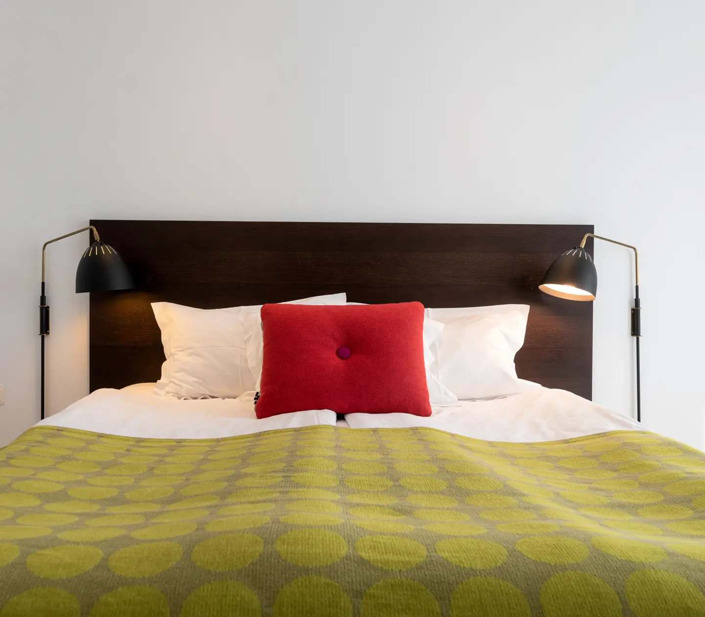 Ljust hotellrum med säng, röd kudde och sänglampor