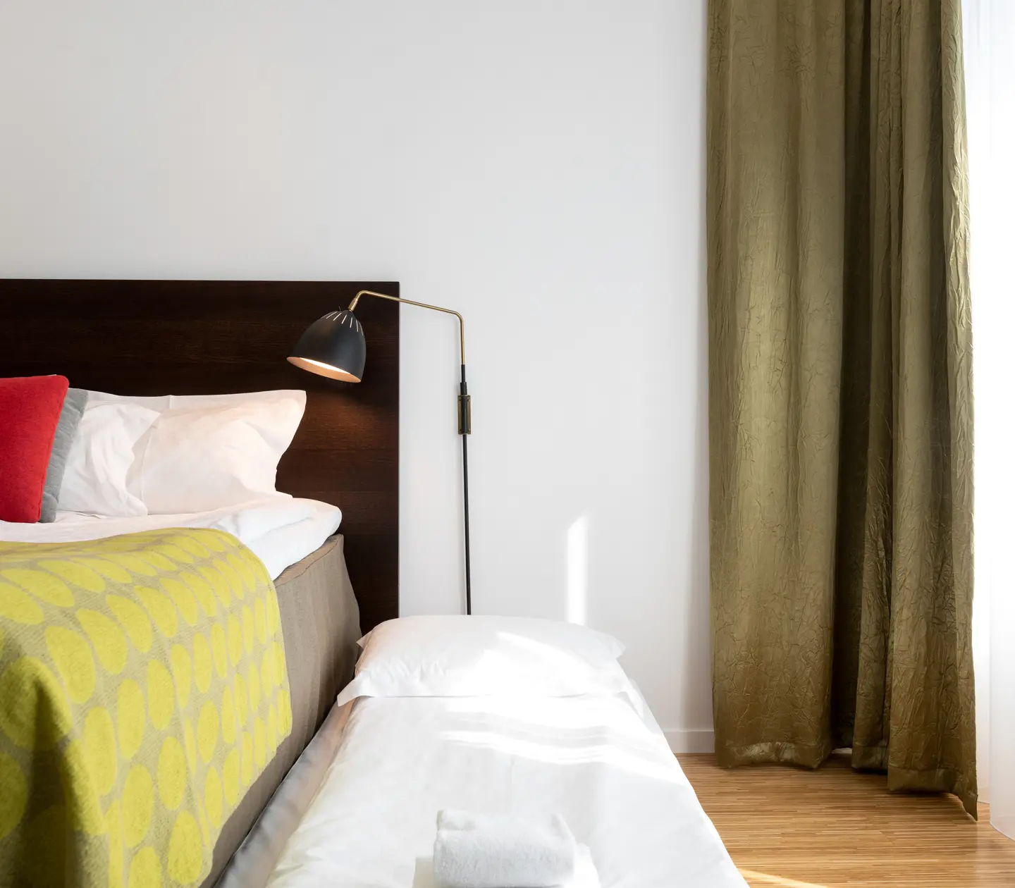 Ljust hotellrum med säng, extrasäng och sänglampa