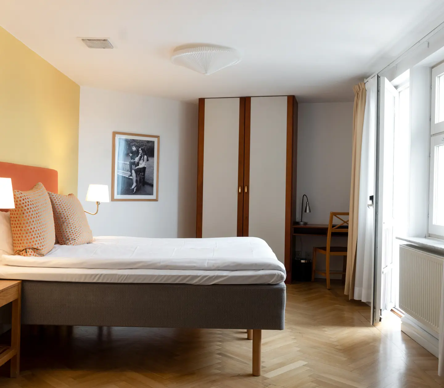 Ljust hotellrum med säng, garderob och sänglampor