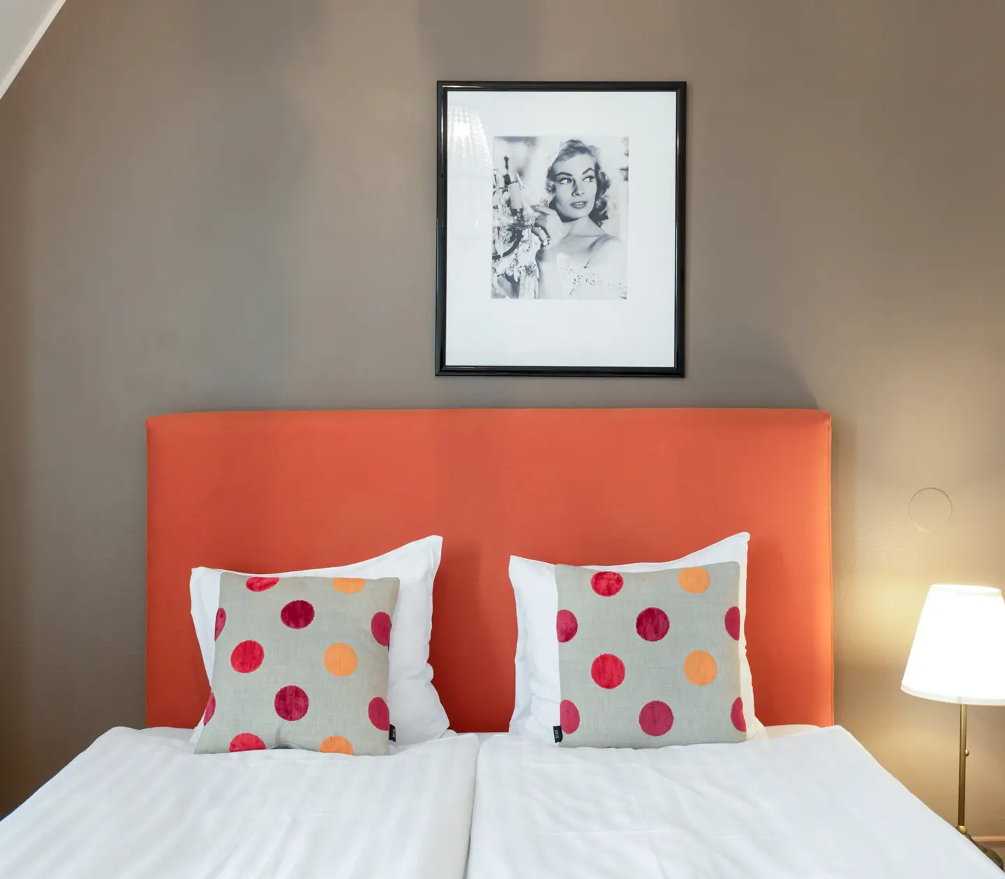 Hotellrum med säng, orange sänggavel och prickiga kuddar