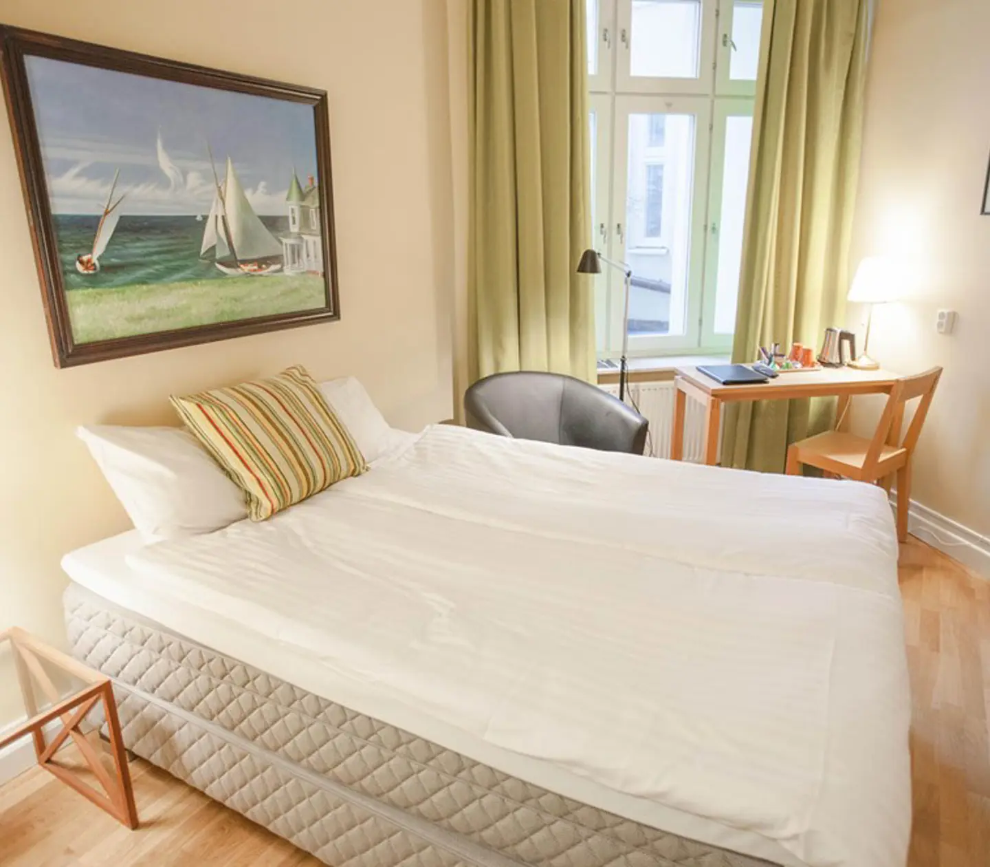 Ljust hotellrum med säng, skrivbord och tavla
