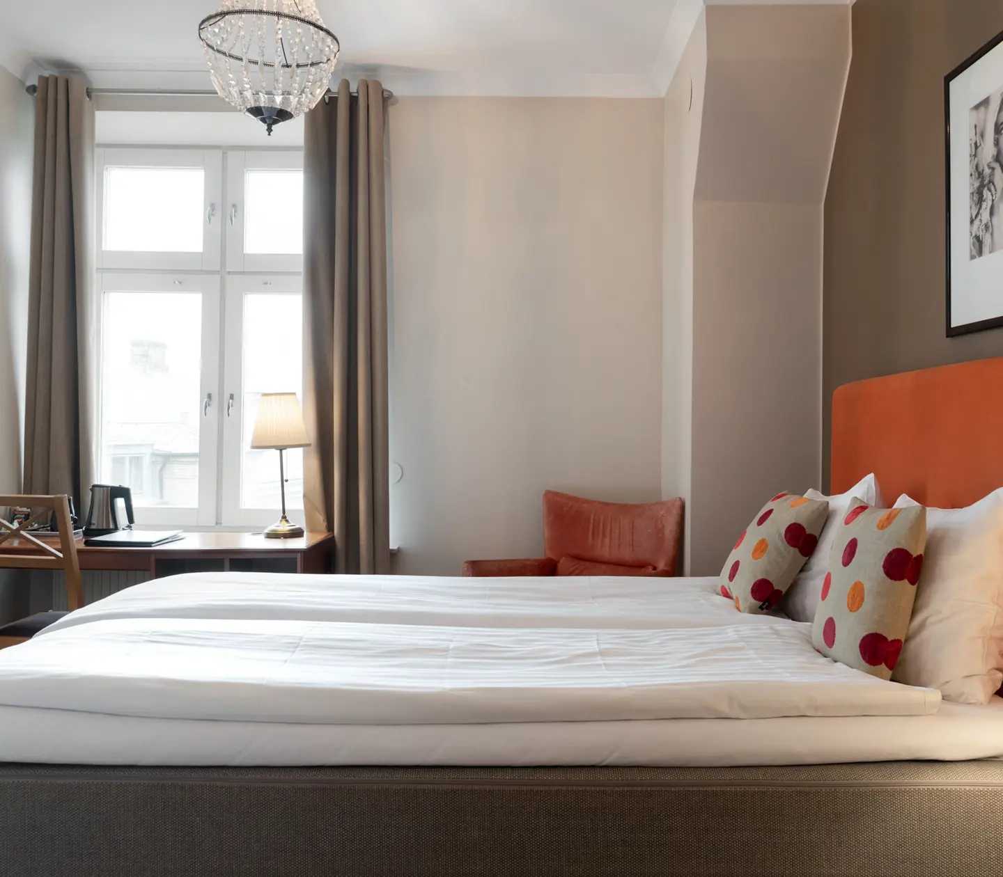 Mysigt hotellrum med säng, orange sänggavel och skrivbord