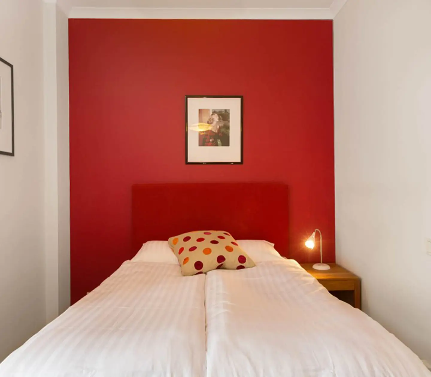 Hotellrum med säng, röd vägg och tavlor