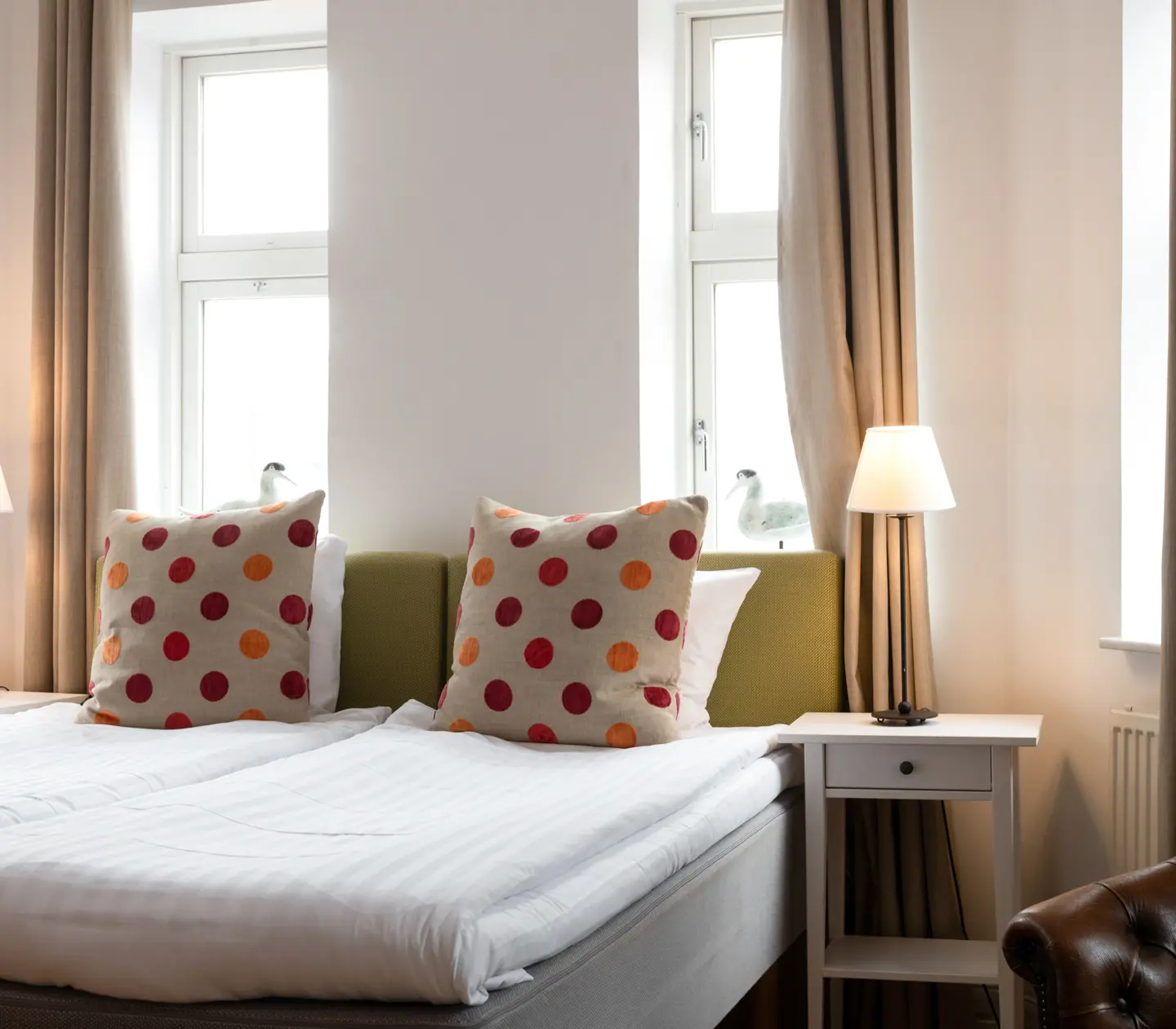 Mysigt hotellrum med säng, grön sänggavel och sänglampor