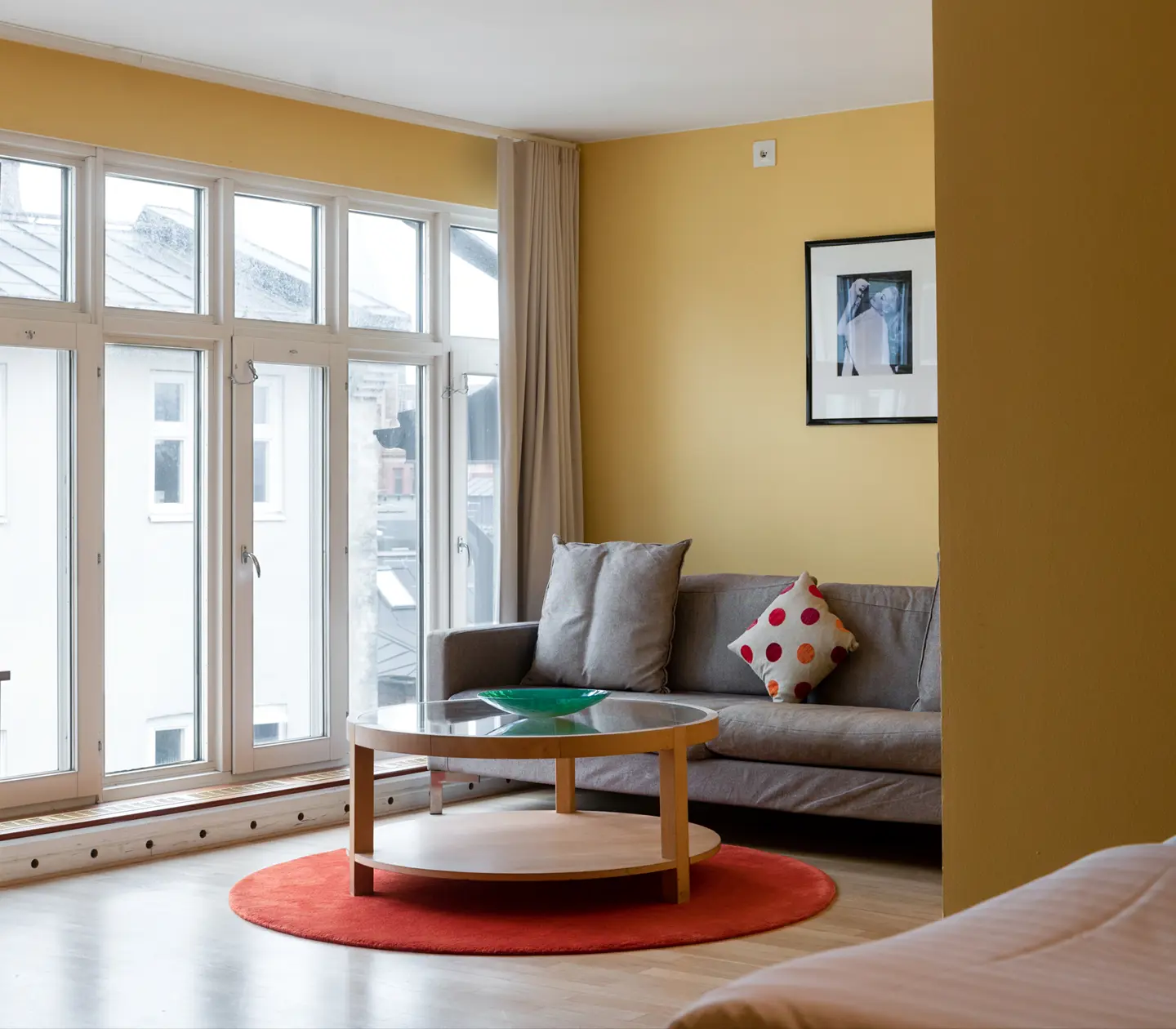 Gult hotellrum med grå soffgrupp, stora fönster och tavla