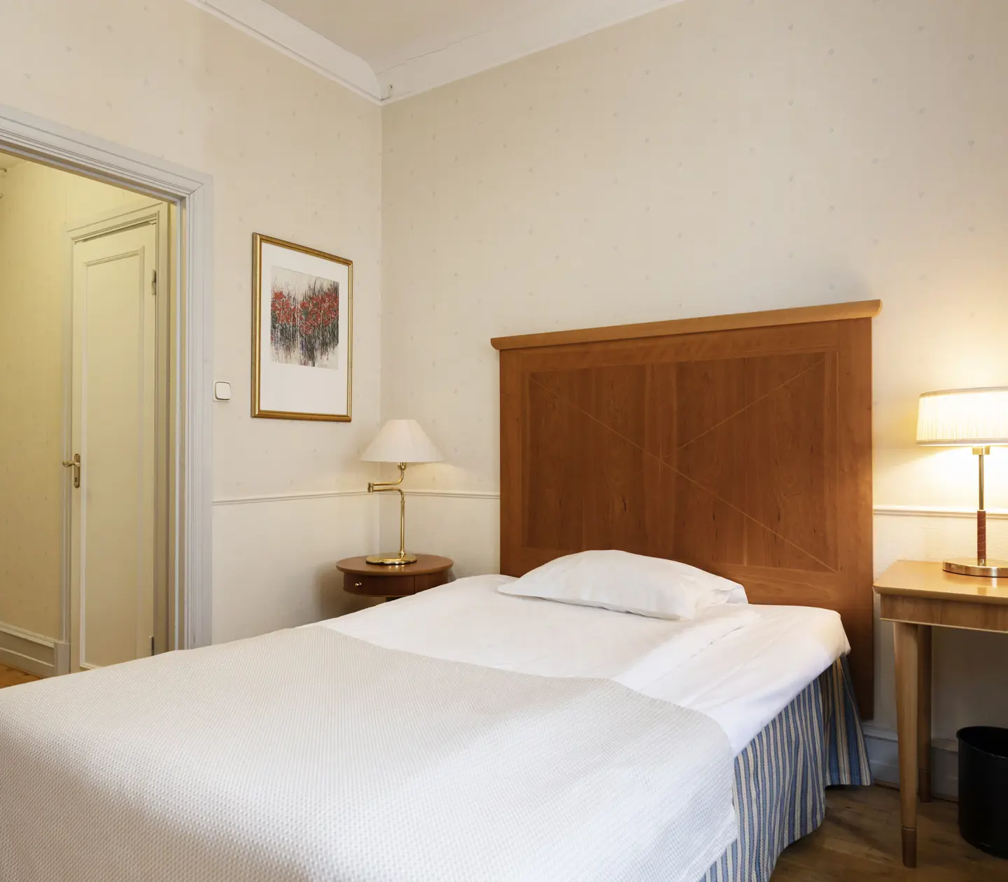Hotellrum med enkelsäng, skrivbord och bordslampor