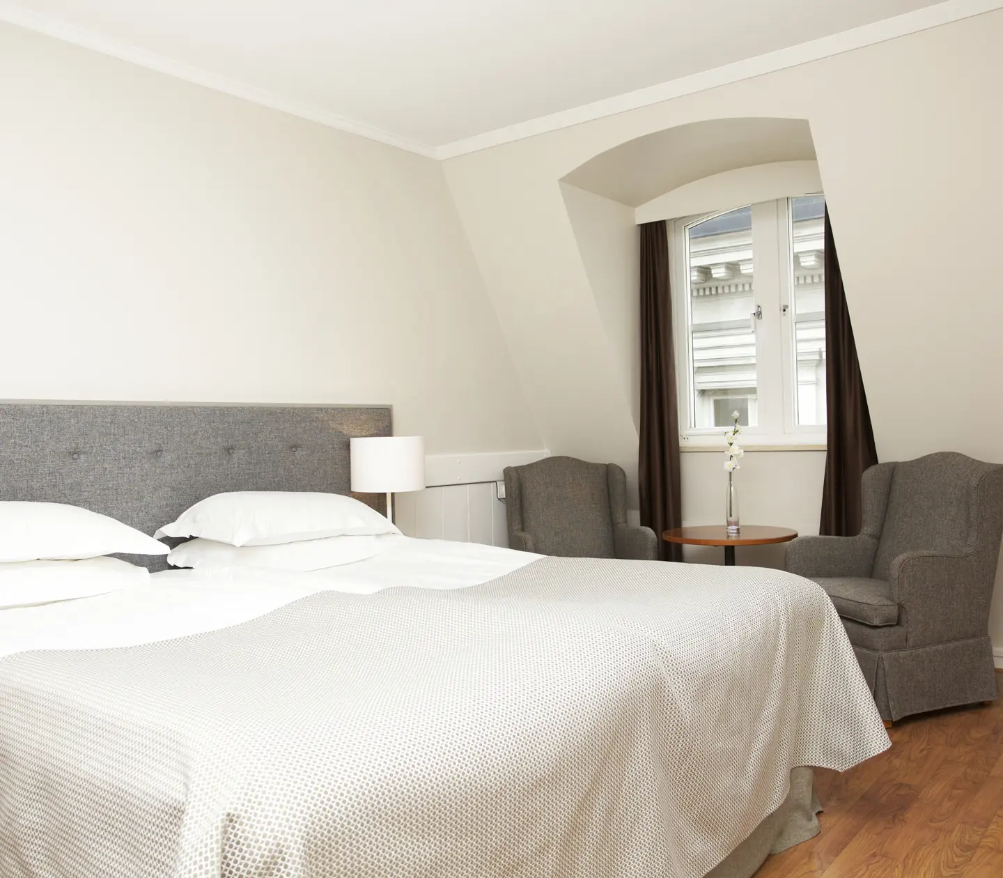 Ljust hotellrum med dubbelsäng, fåtöljer och fönster