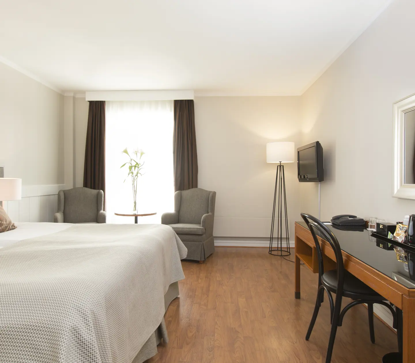 Ljust hotellrum med dubbelsäng, skrivbord och fåtöljer