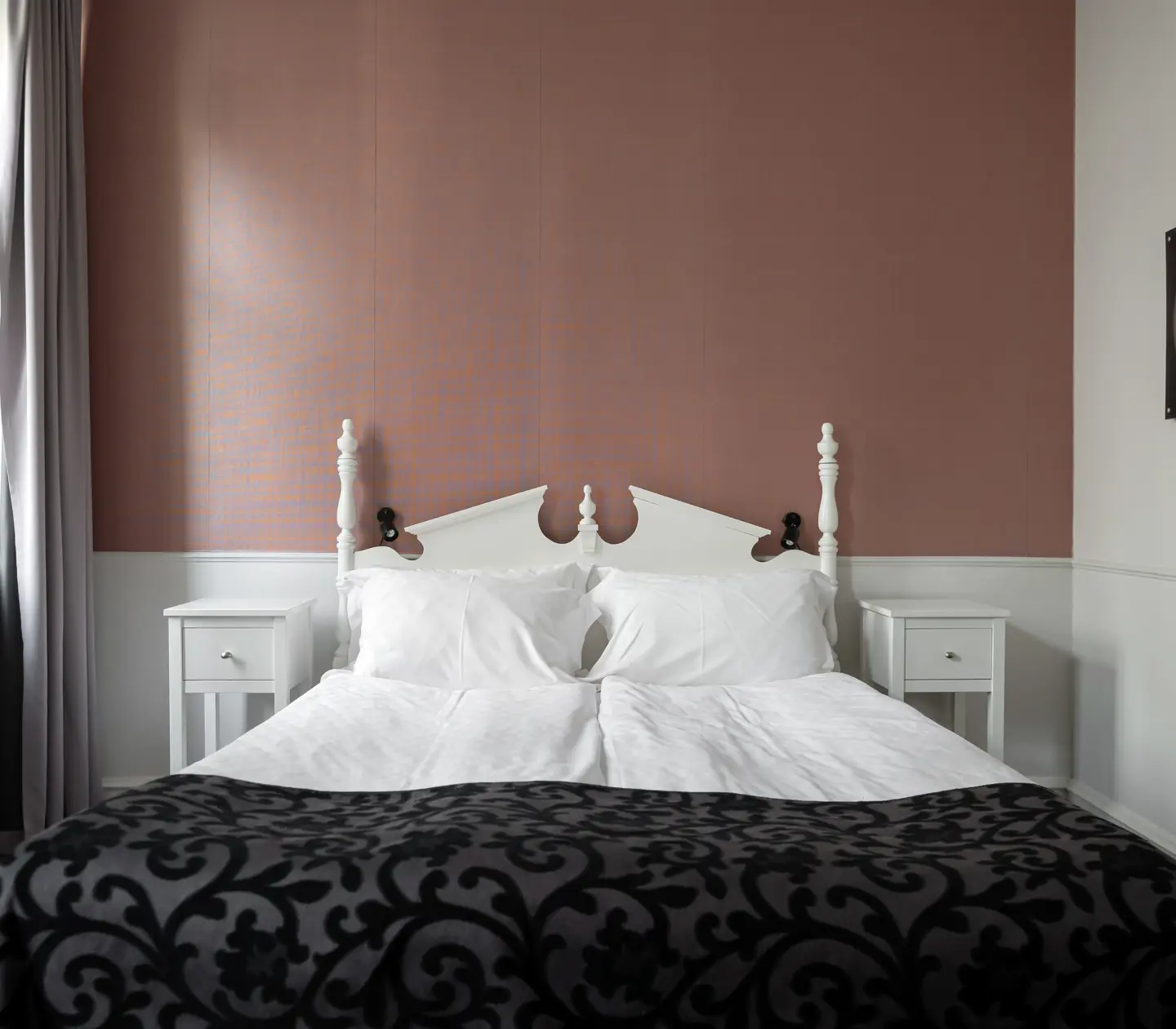 Hotellrum med rosa tapet, dubbelsäng och nattduksbord