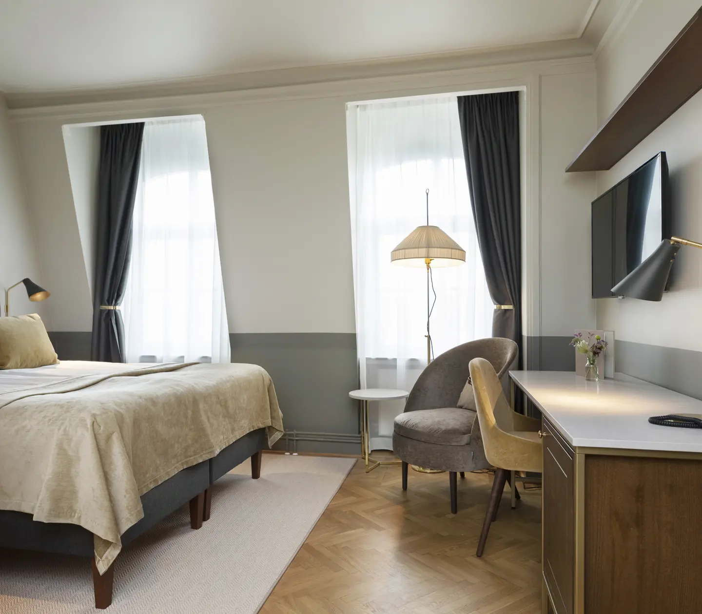Ljust hotellrum med dubbelsäng, skrivbord, fåtölj och fönster