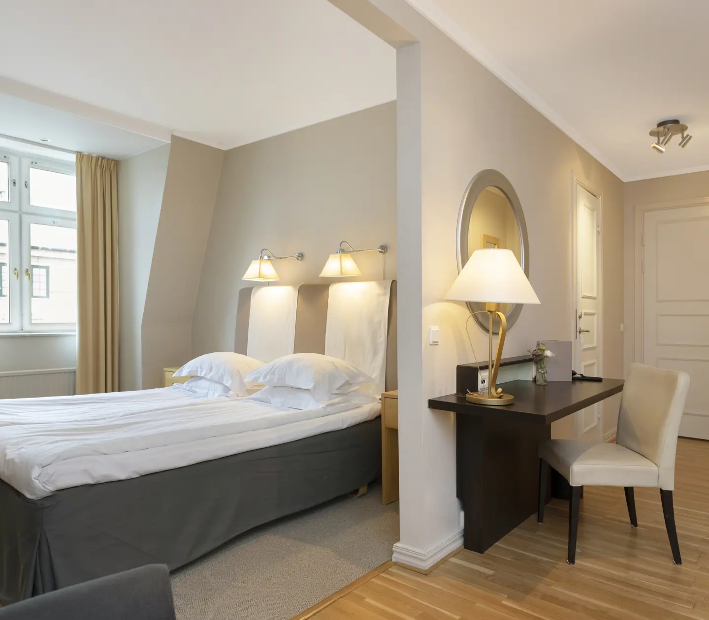 Ljust hotellrum med dubbelsäng, skrivbord och fönster