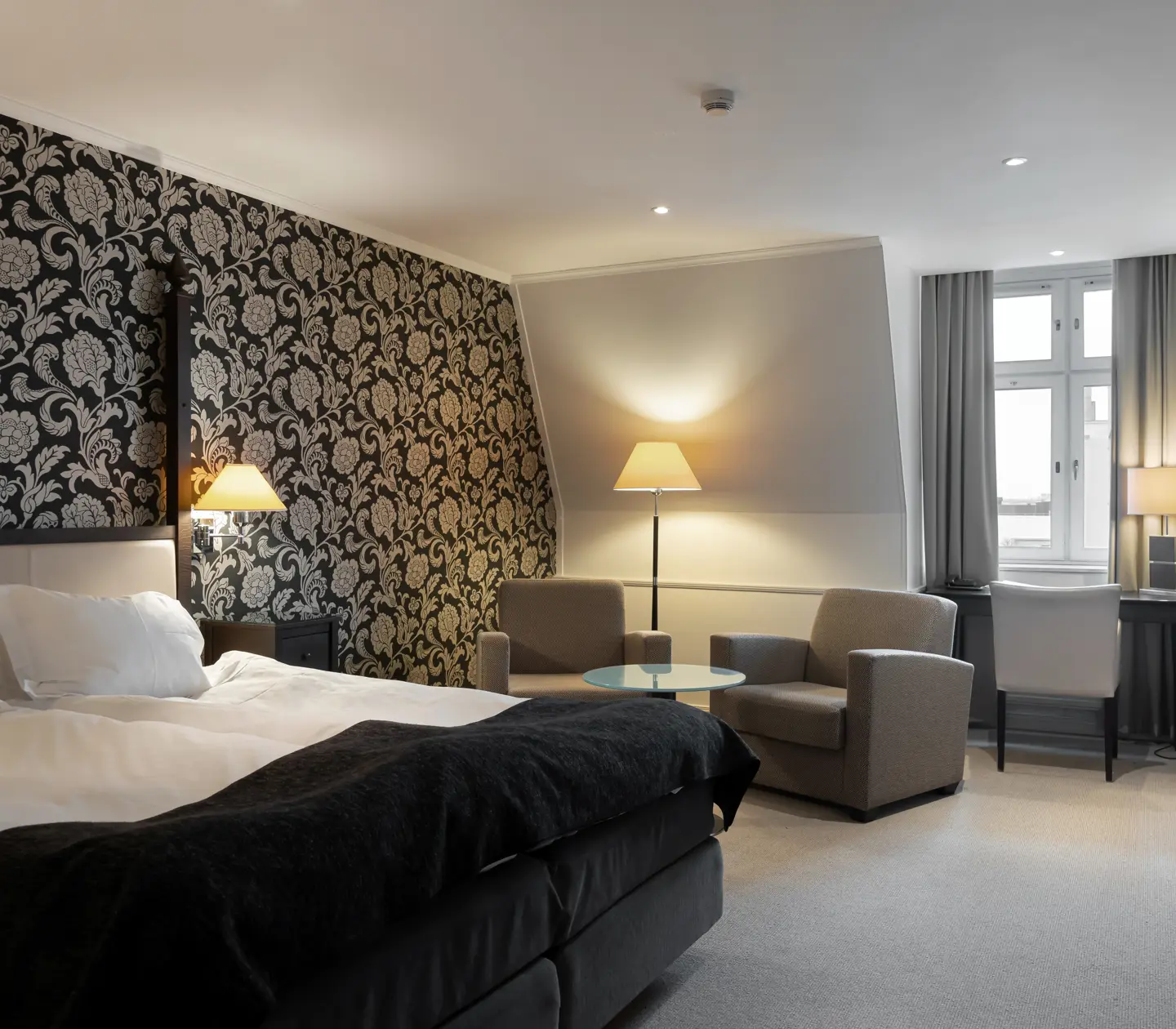 Fint hotellrum med fondtapet, dubbelsäng, skrivbord och fåtöljer