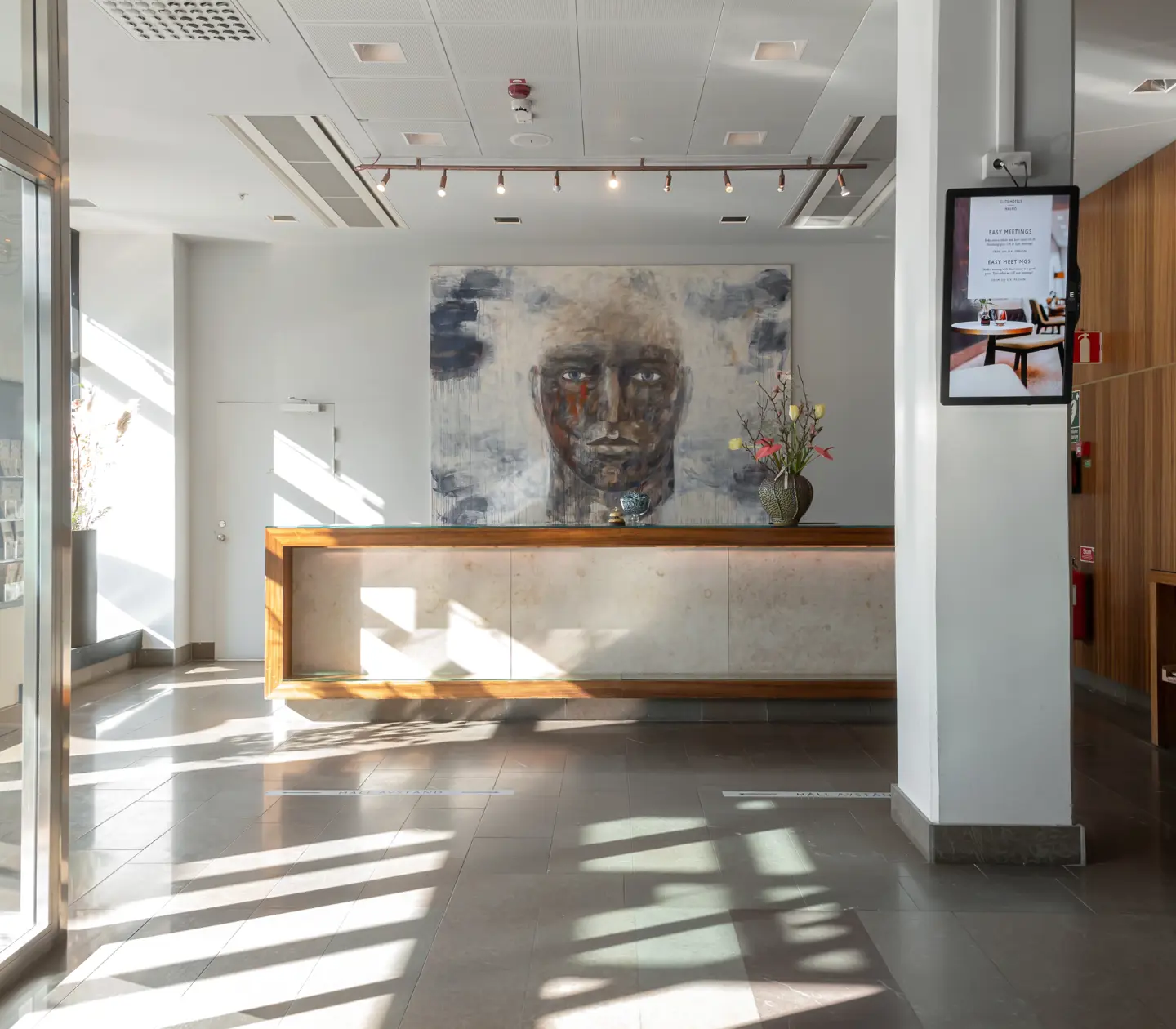 Hotellobby med receptionsdisk och stor målning av ansikte
