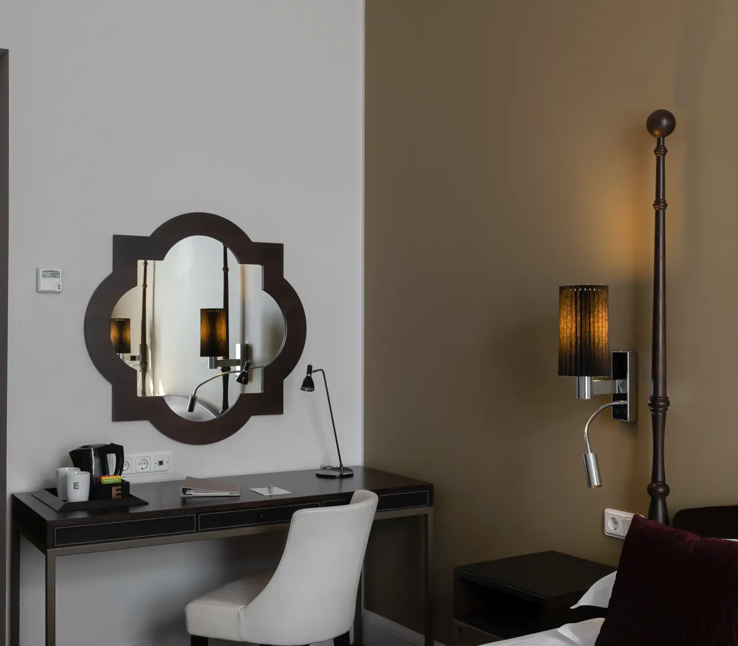 Ljust hotellrum med skrivbord, spegel och sänglampa