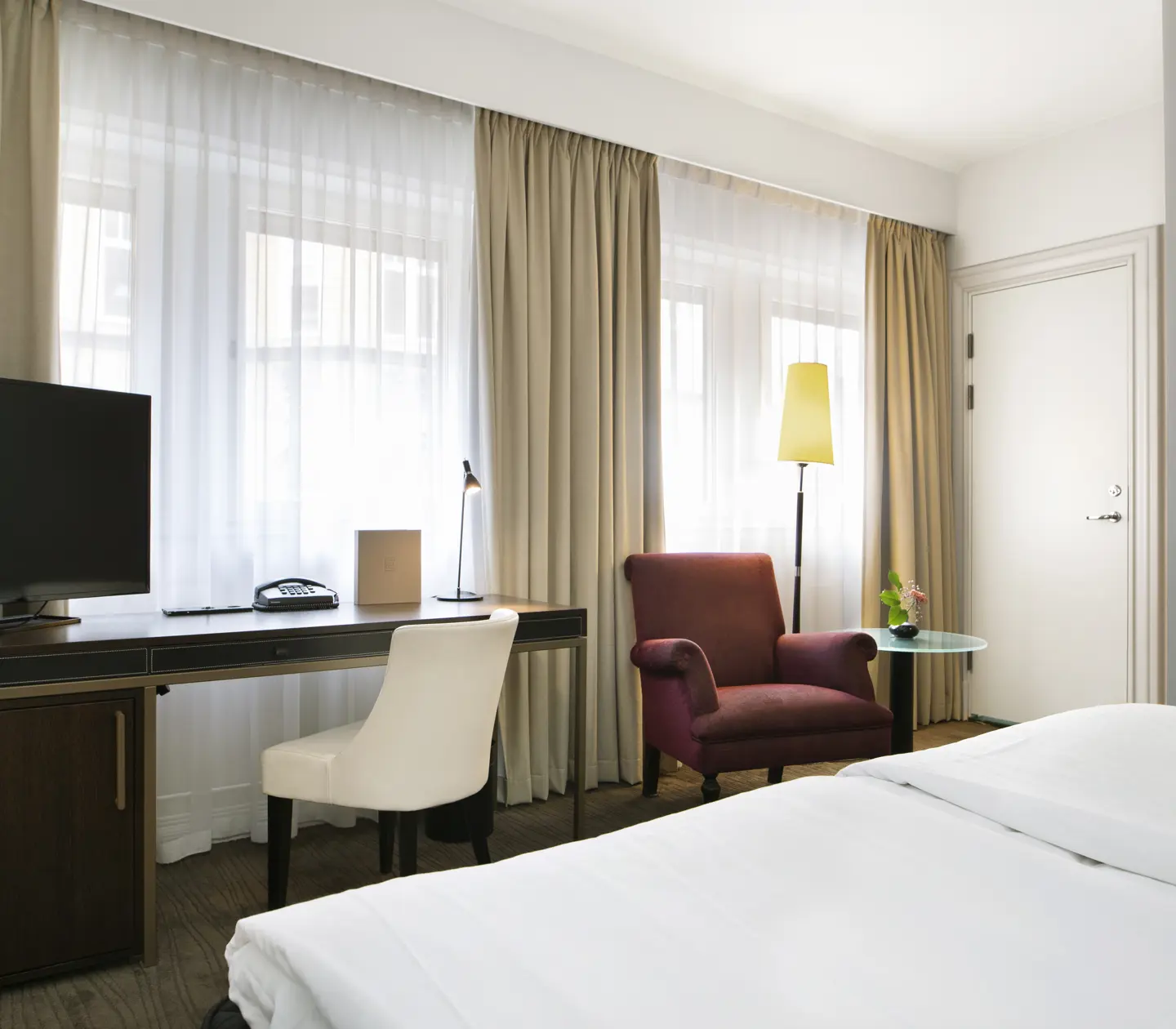 Ljust hotellrum med säng, skrivbord och fönster