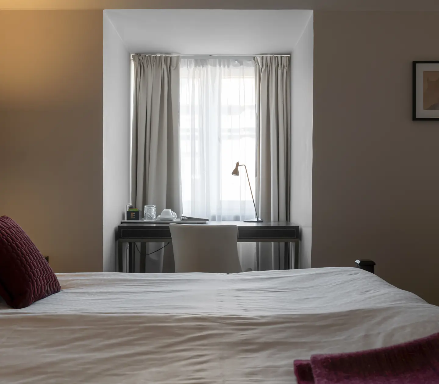 Ljust hotellrum med säng, skrivbord och sänglampa