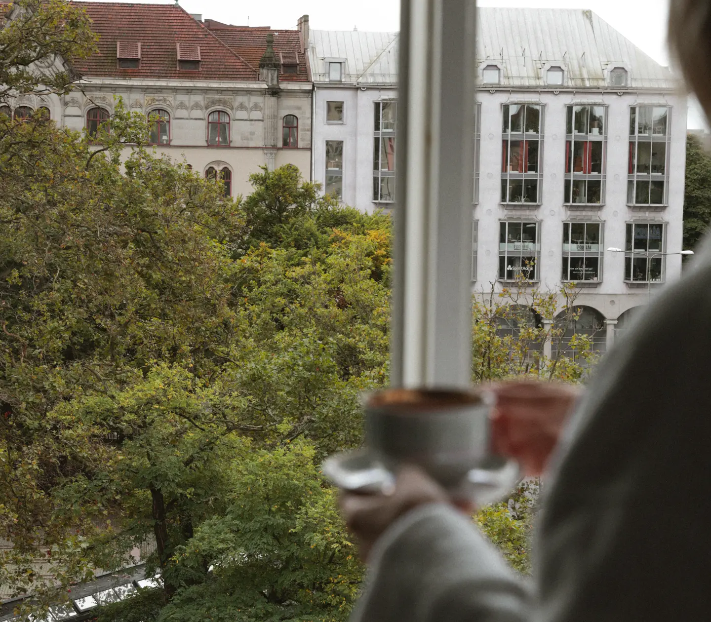 Kvinna som står vid fönster med kaffekopp i handen och tittar ut över utsikt