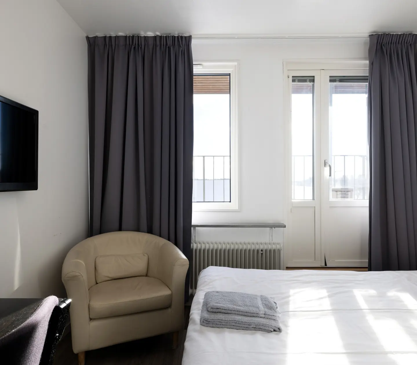 Hotellrum med säng, beige läderfåtölj och tv